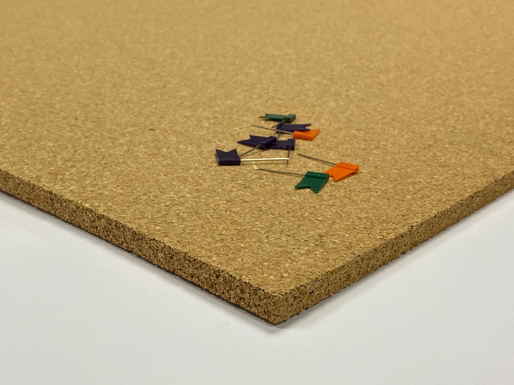 Korktafel mit verstreuten, flaggenförmigen Reißnägeln in Grün, Orange und Lila. Die Oberfläche ist hellbraun.