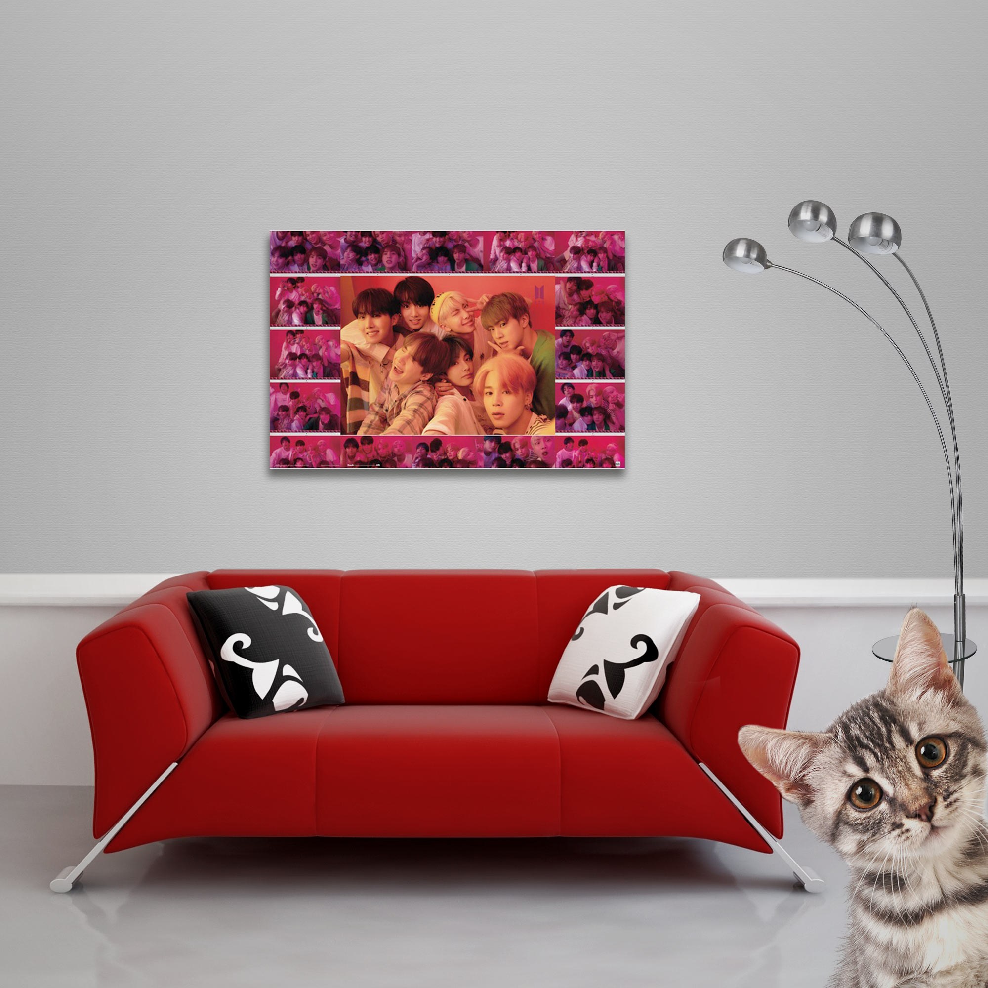 Ein rotes Sofa mit Kissen und eine gerahmte Collage von Menschen. Eine Katze lugt von rechts.