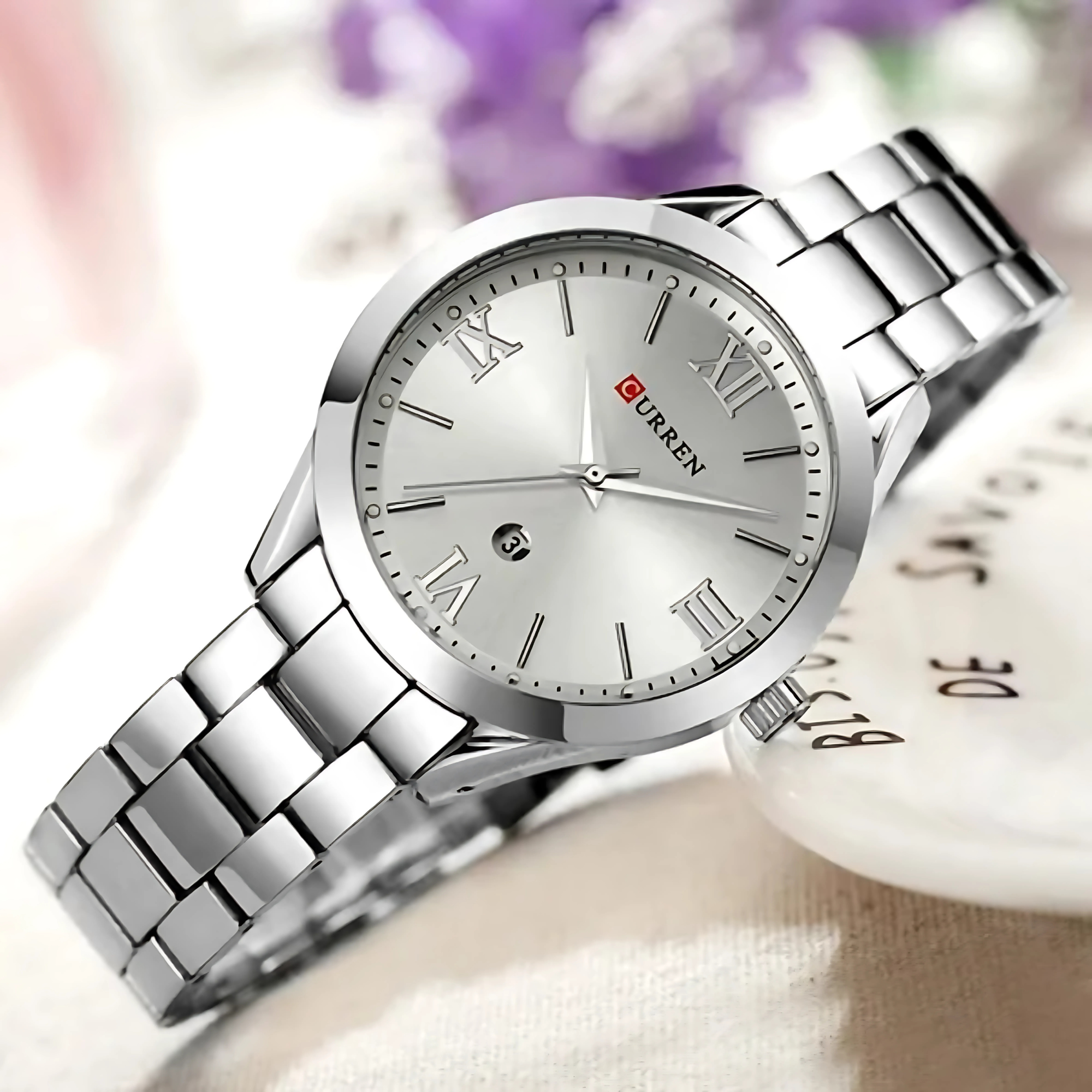 Silberne Uhr mit römischen Ziffern auf dem Zifferblatt und einem silbernen Kettengliederarmband. Auf weißem Untergrund.
