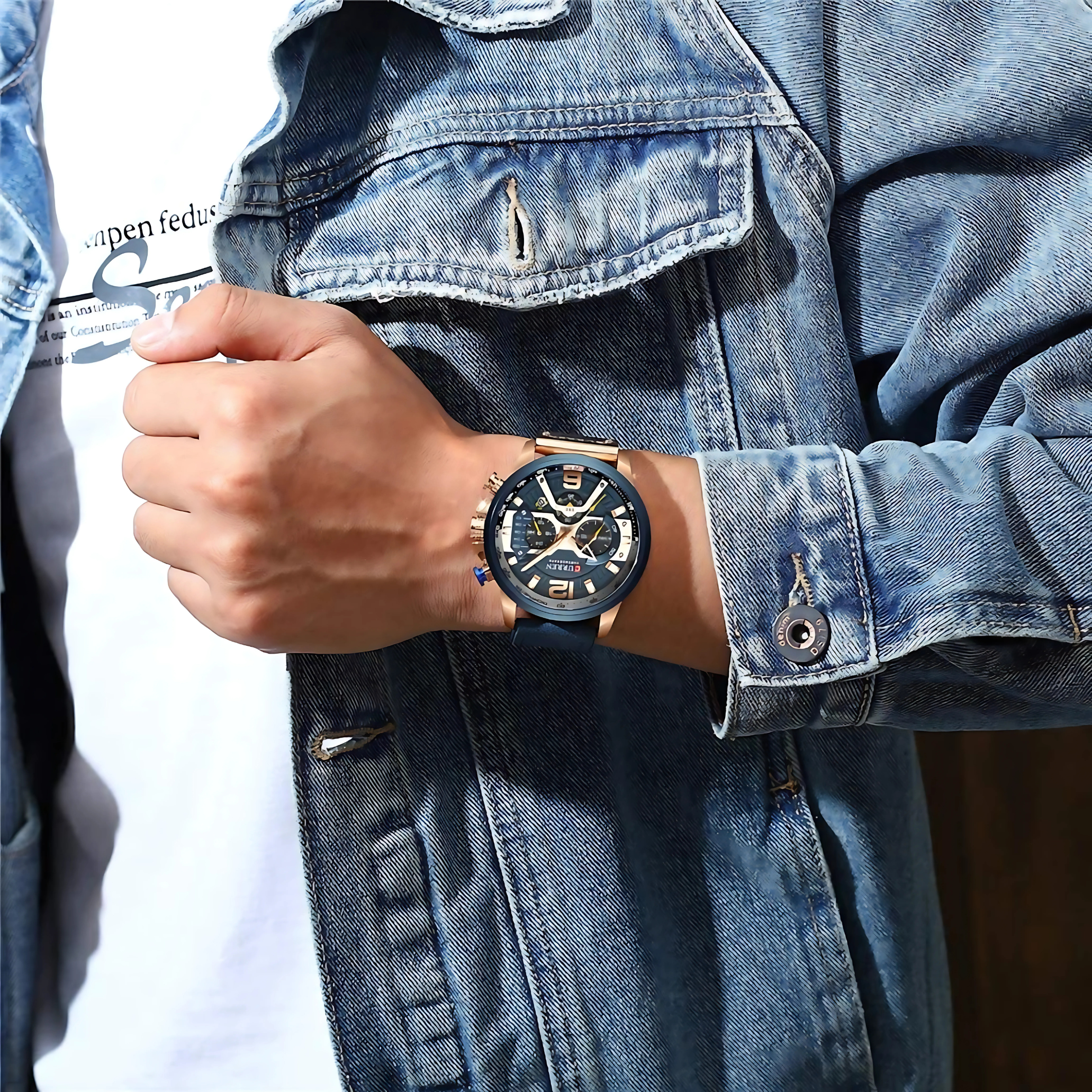 Ein Mann trägt eine Jeansjacke und eine Uhr. Die Uhr hat ein blaues Zifferblatt und goldfarbene Akzente.