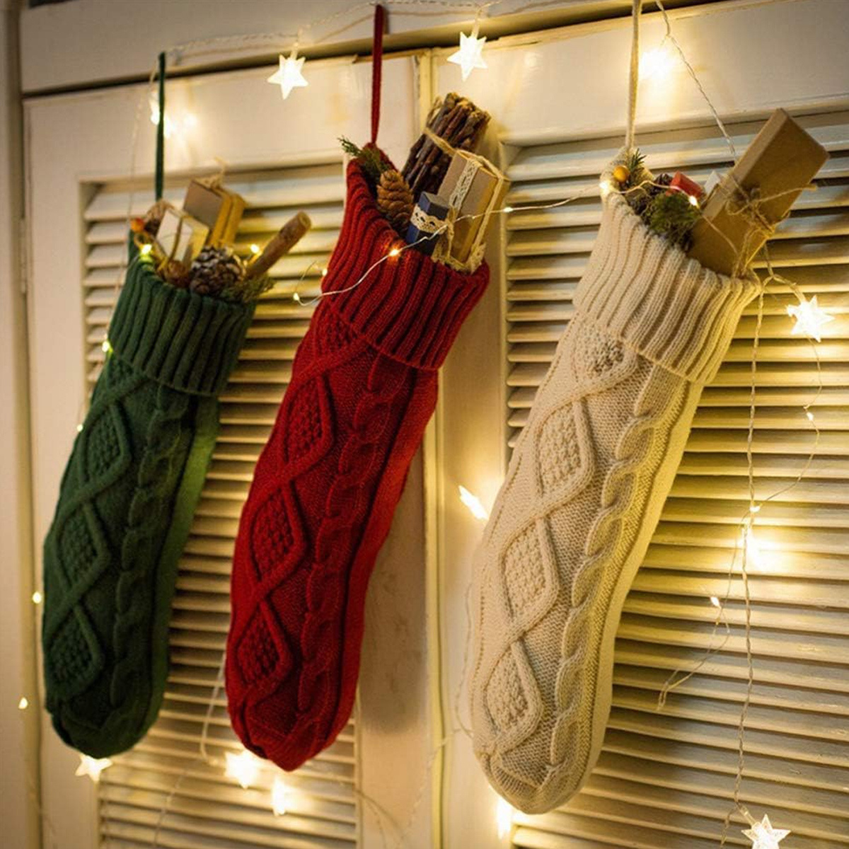 Drei Weihnachtsstrümpfe hängen vor einer weißen Fensterladentür mit Sternen.