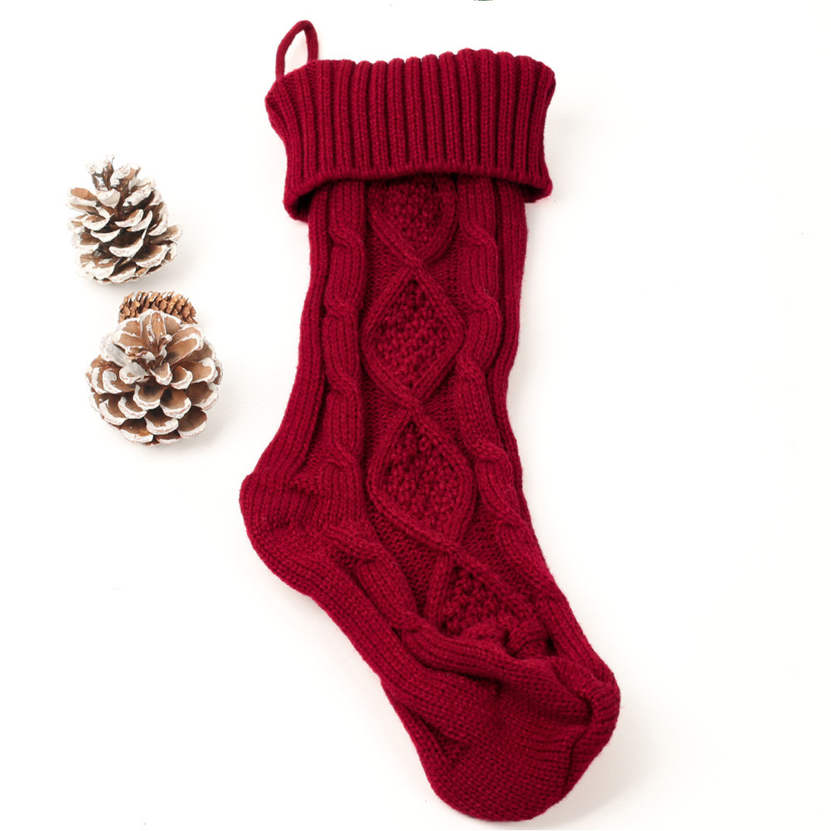 Ein roter Weihnachtsstrumpf mit Zopfmuster und zwei Tannenzapfen.