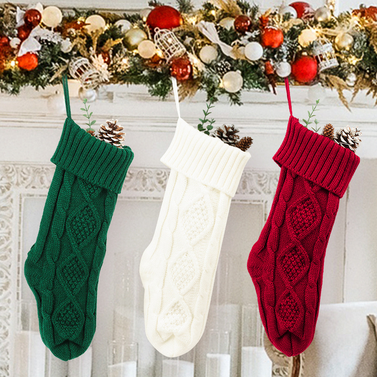 Drei Weihnachtssocken hängen. Grün, weiß und rot. Alle enthalten Tannenzapfen und hängen an einer Girlande.
