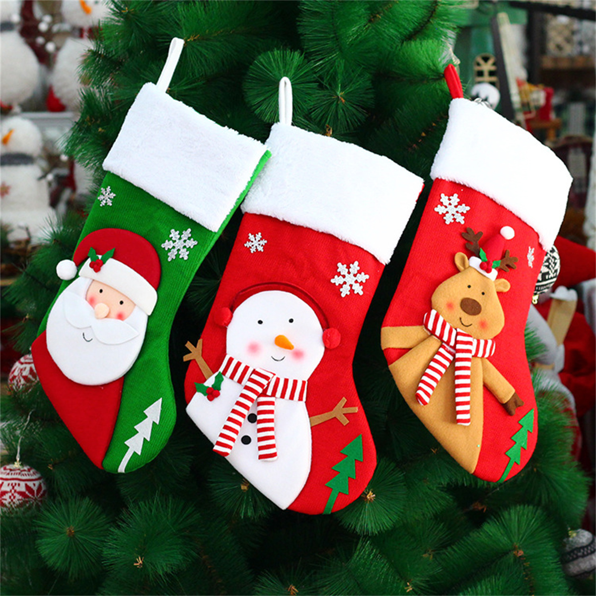 Drei Weihnachtssocken mit Weihnachtsmann, Schneemann und Rentier hängen an einem Weihnachtsbaum.