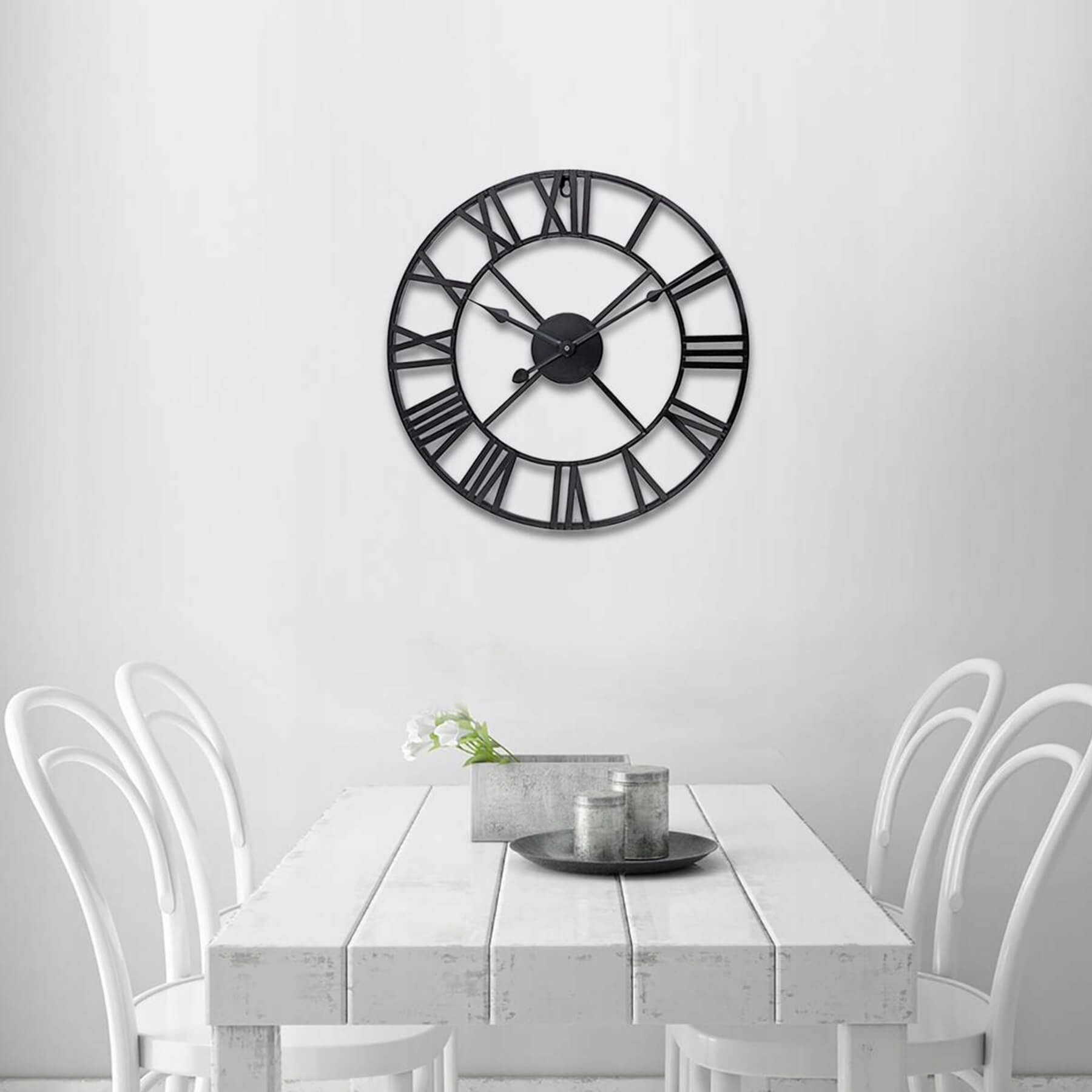 Eine schwarze, runde Wanduhr mit römischen Ziffern, über einem weißen Tisch.