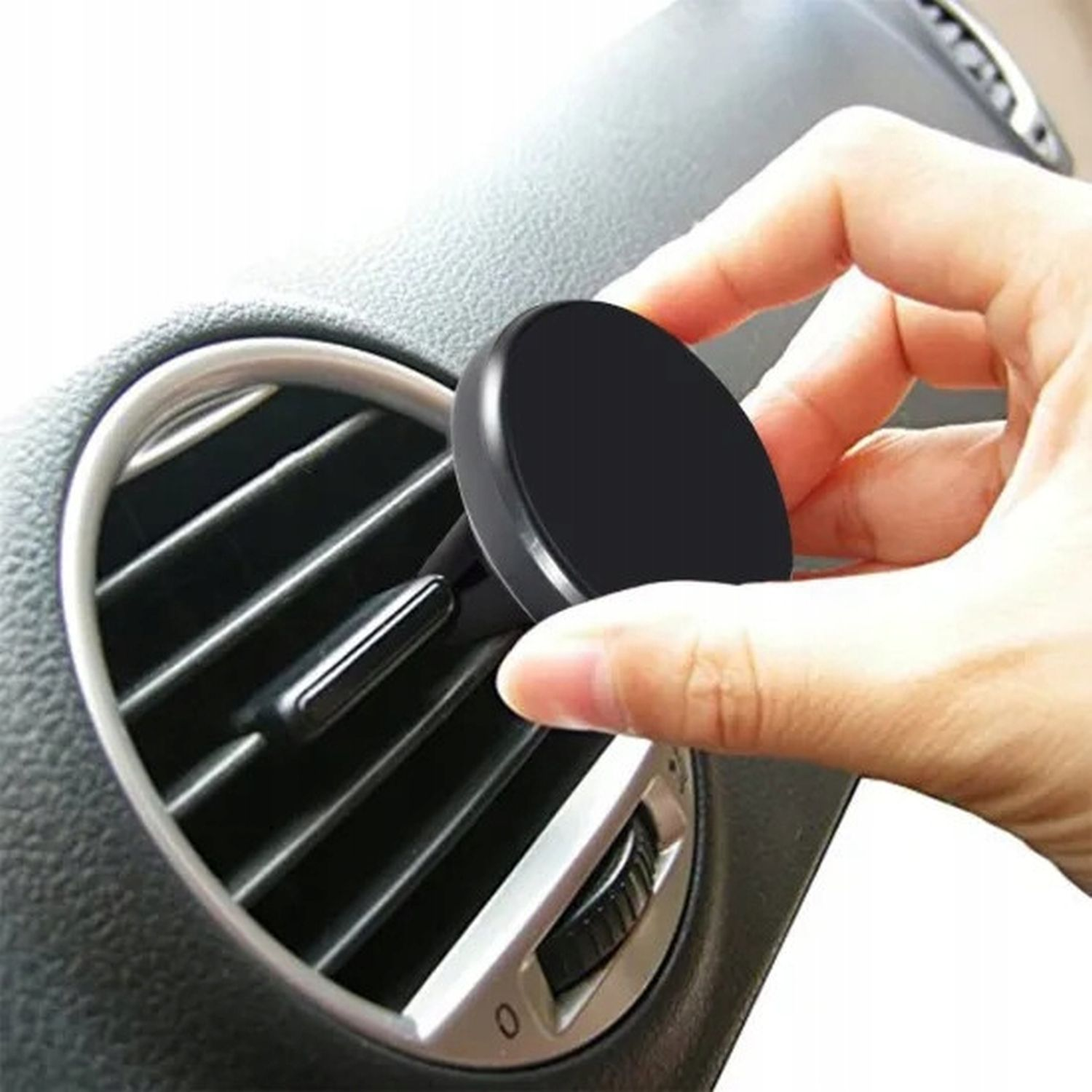 Eine Hand platziert eine schwarze runde Telefonhalterung in der Lüftungsöffnung eines Autos.