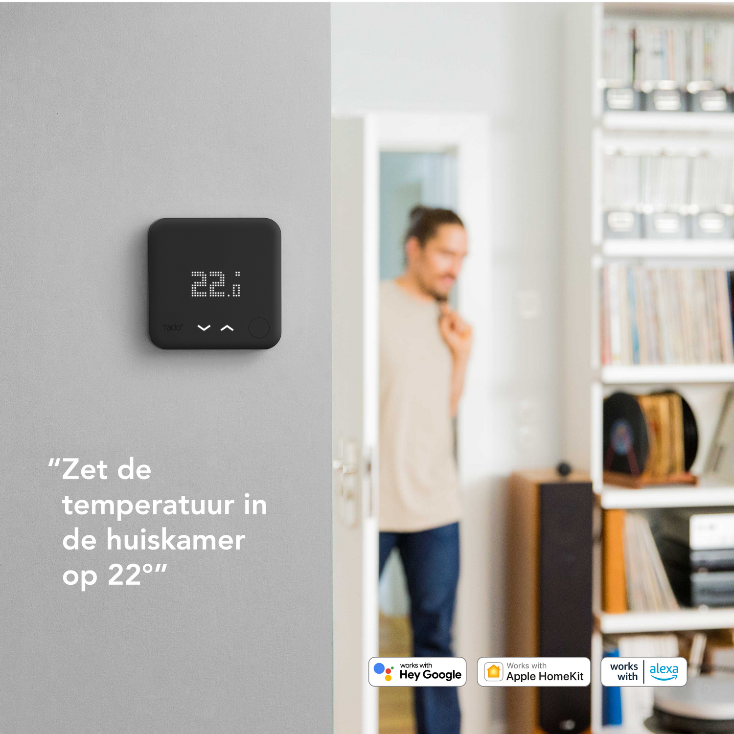 Ein intelligenter Thermostat an einer Wand mit niederländischem Text und eine Person im Hintergrund.
