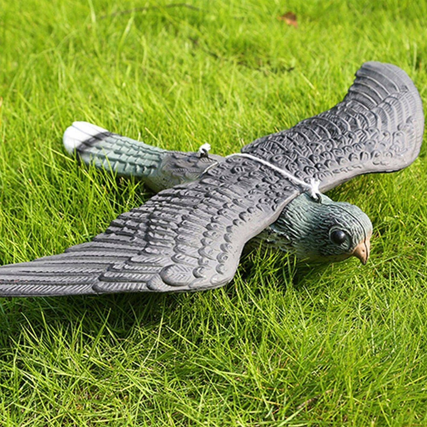 Un'esca per uccelli in plastica su erba verde. Le ali sono estese. È attaccato uno spago bianco.
