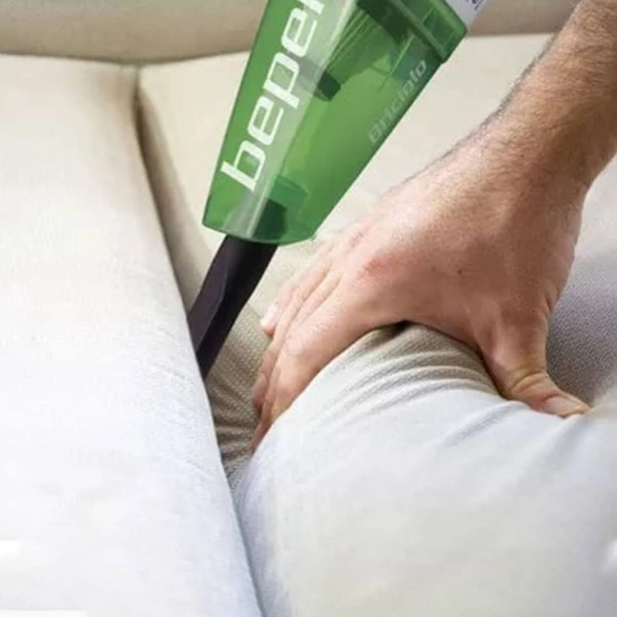 Mano che usa un aspirapolvere portatile su un divano bianco. Aspirapolvere verde, sfondo bianco.