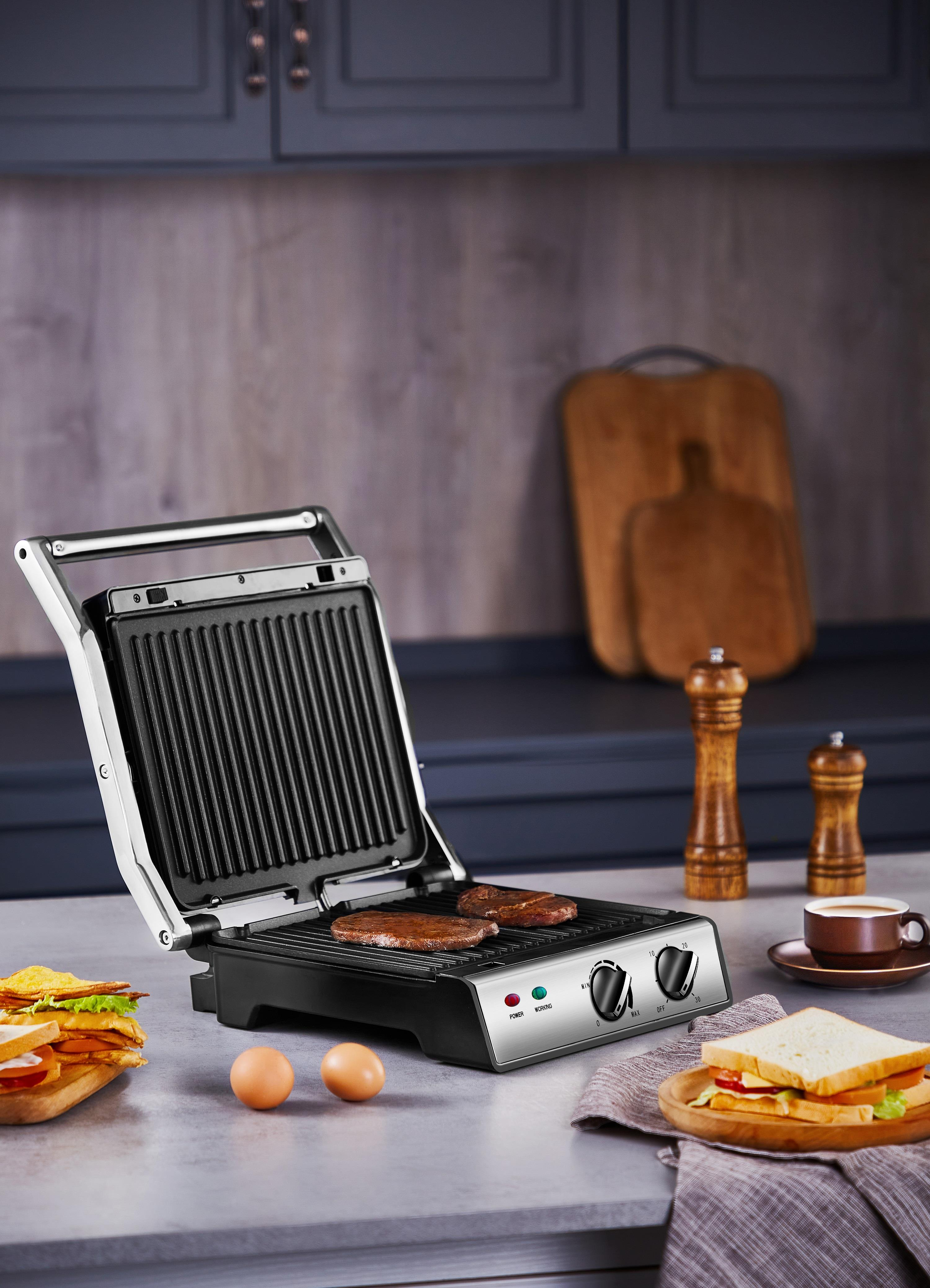 Ein offener Grill mit Essen, mit Schneidebrettern und anderen Gegenständen drumherum, auf einer grauen Arbeitsplatte. Zwei Eier sind vorhanden.