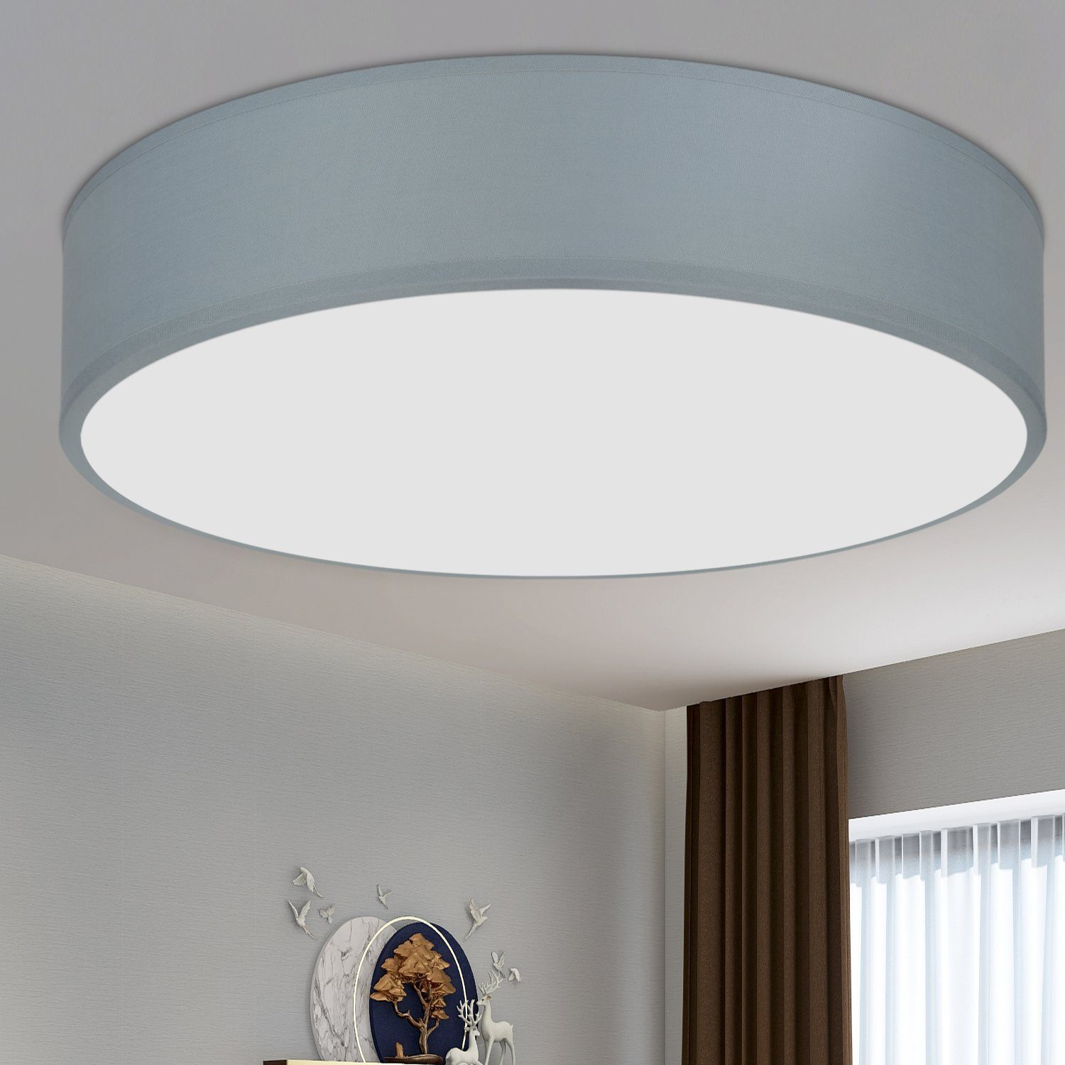 Una lámpara de techo redonda gris con centro blanco, con decoración y una cortina marrón al fondo.