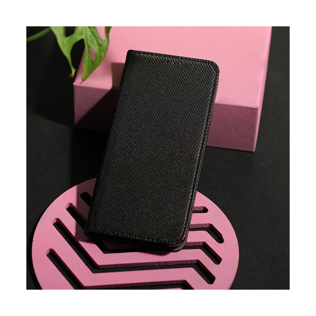 Custodia nera per telefono su vassoio rosa. Una foglia verde sullo sfondo.