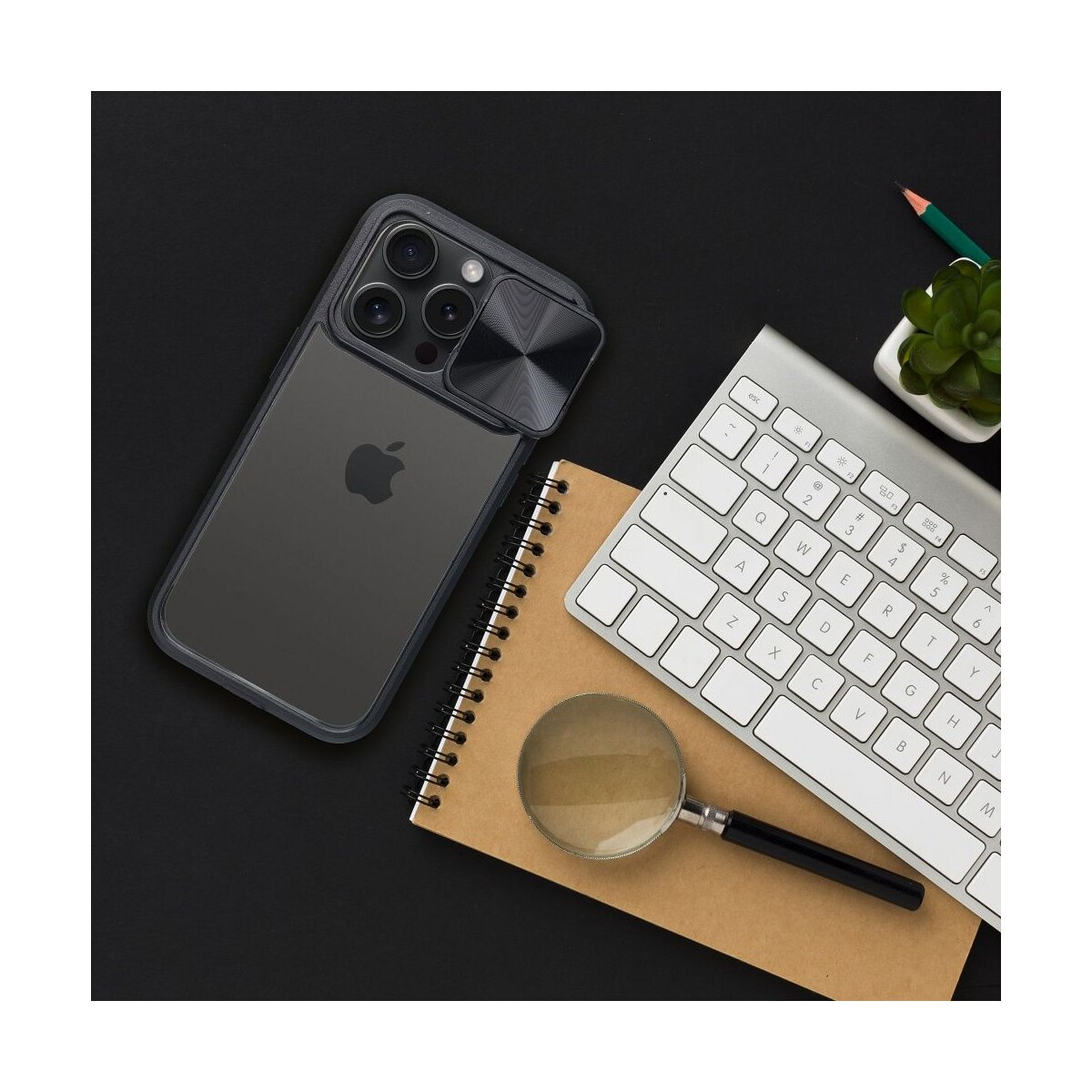 Un telefono in una custodia, quaderno, tastiera, lente d'ingrandimento e penna su una superficie nera.