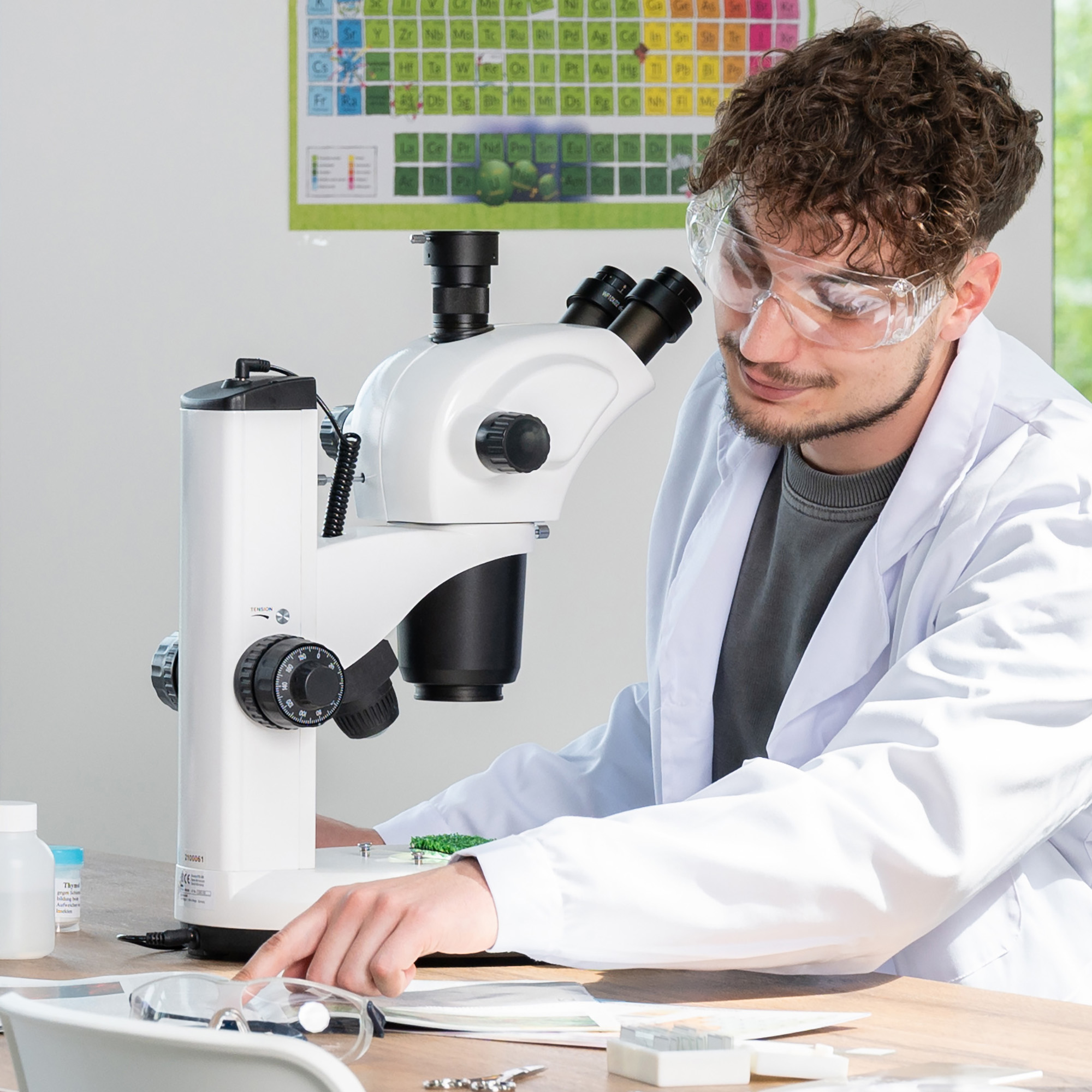 Científico usando un microscopio, con gafas y bata de laboratorio.