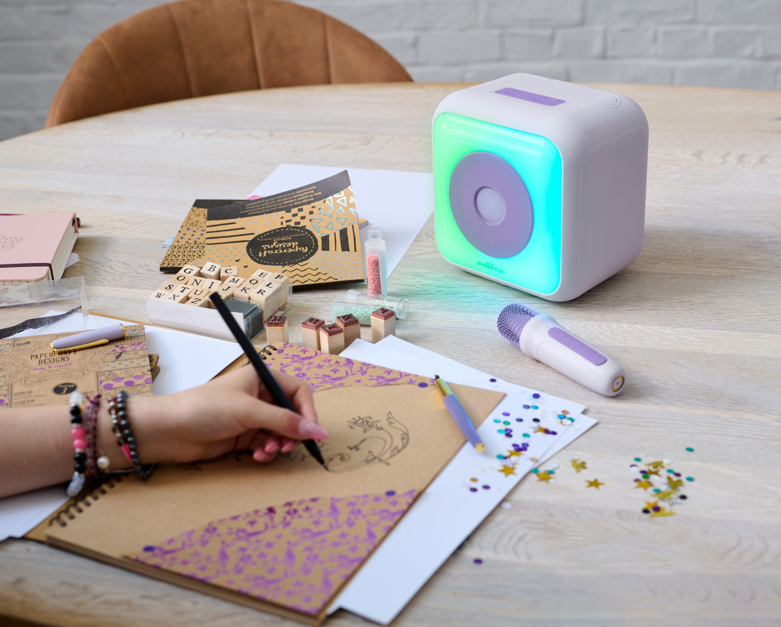 Una persona dibuja en un cuaderno, y un altavoz blanco en una mesa de madera.