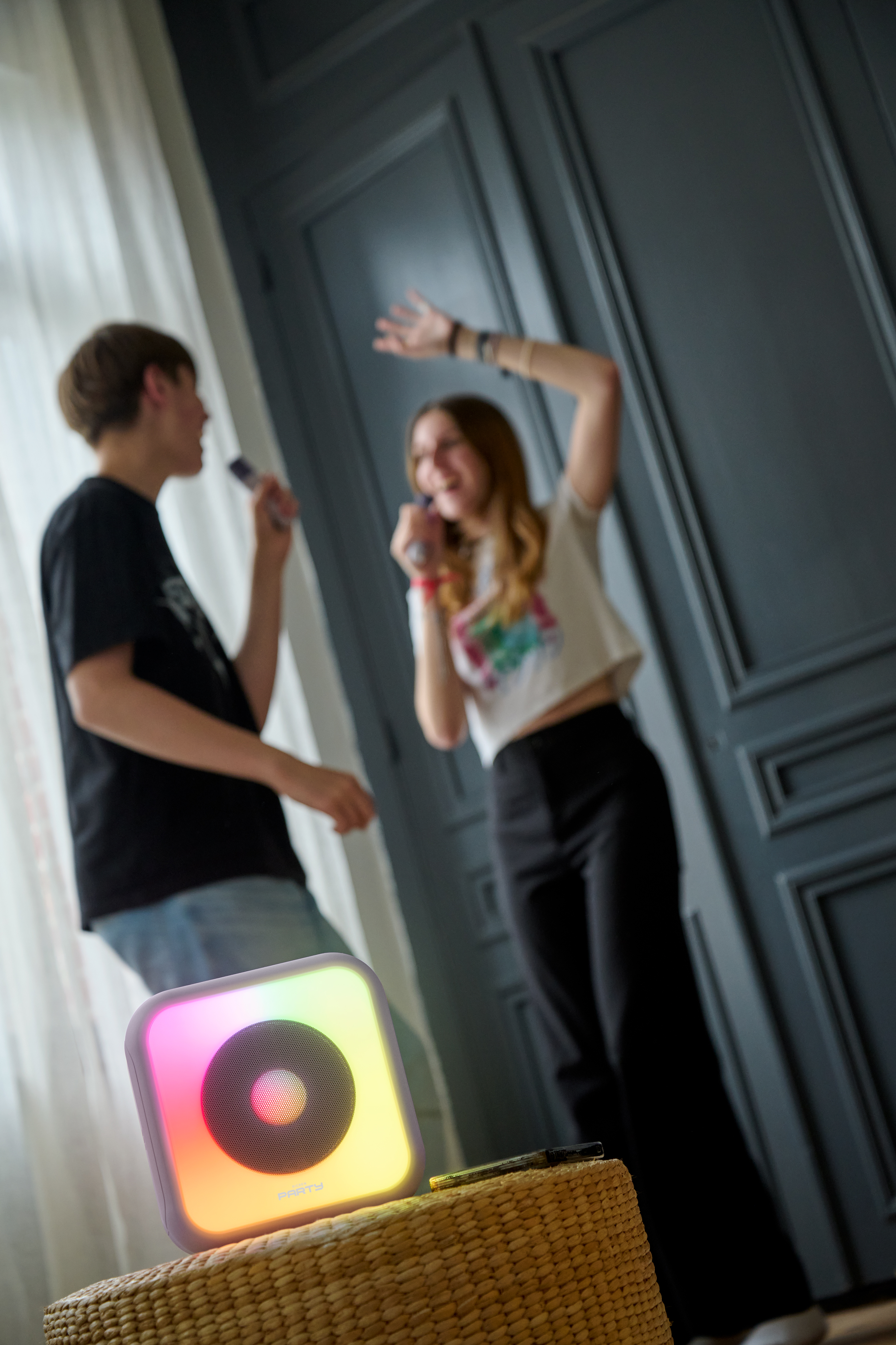 Dos personas cantando en micrófonos cerca de un altavoz iluminado. Cesta de mimbre en primer plano.