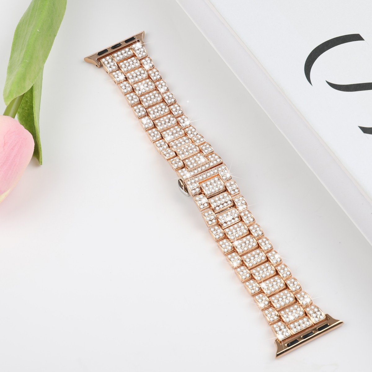 Roségoldenes Uhrenarmband mit vielen kleinen, funkelnden, klaren Kristallen. Es liegt auf einer weißen Oberfläche.
