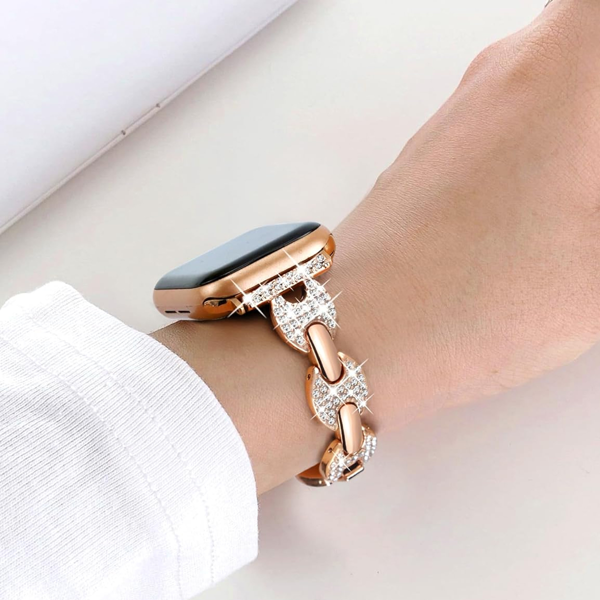 Eine goldene Uhr mit einem roségoldenen Armband mit Diamanten am Handgelenk. Ein weißes Hemd im Hintergrund.