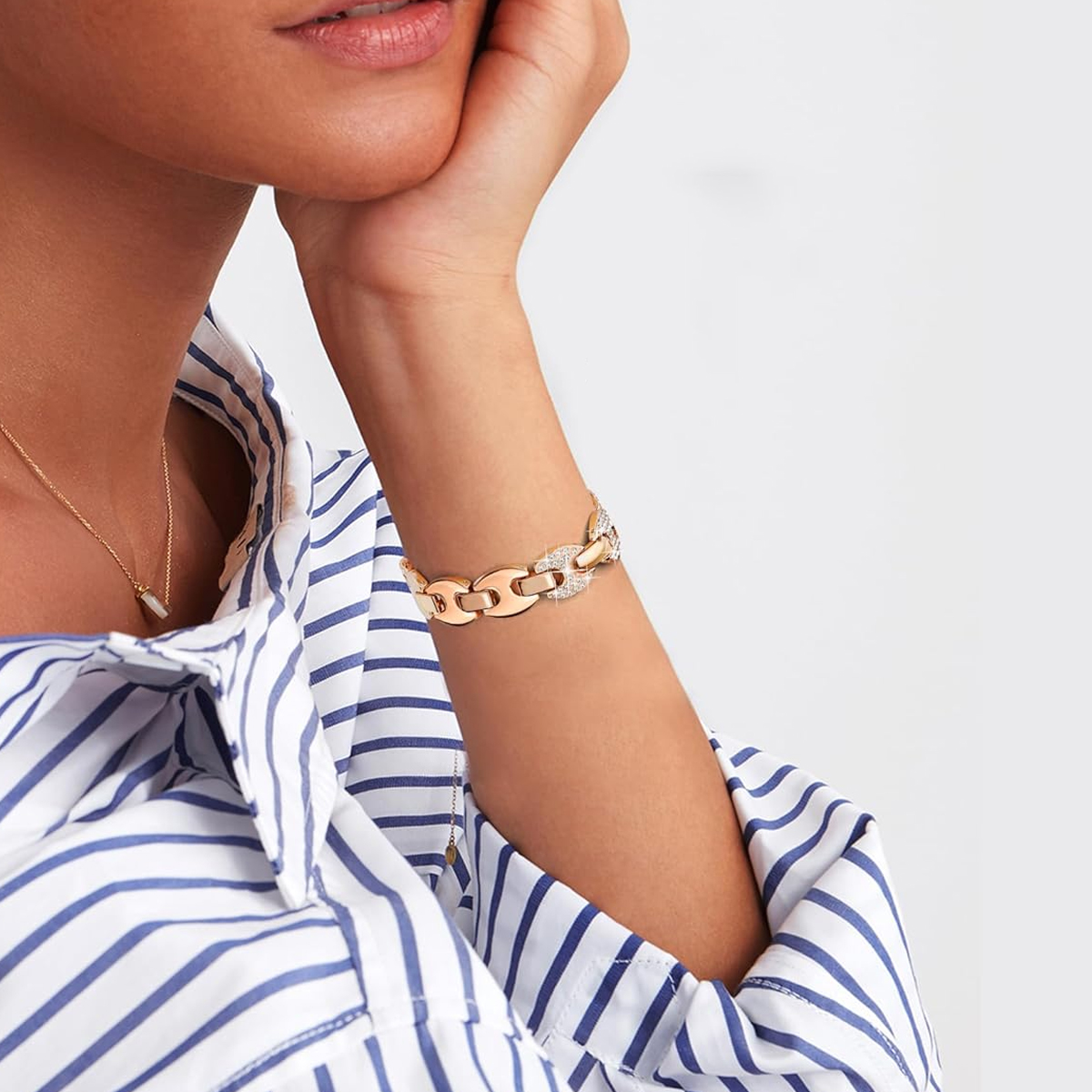 Nahaufnahme eines Arms einer Frau mit goldenem Armband, weiß-blau gestreiftes Hemd.