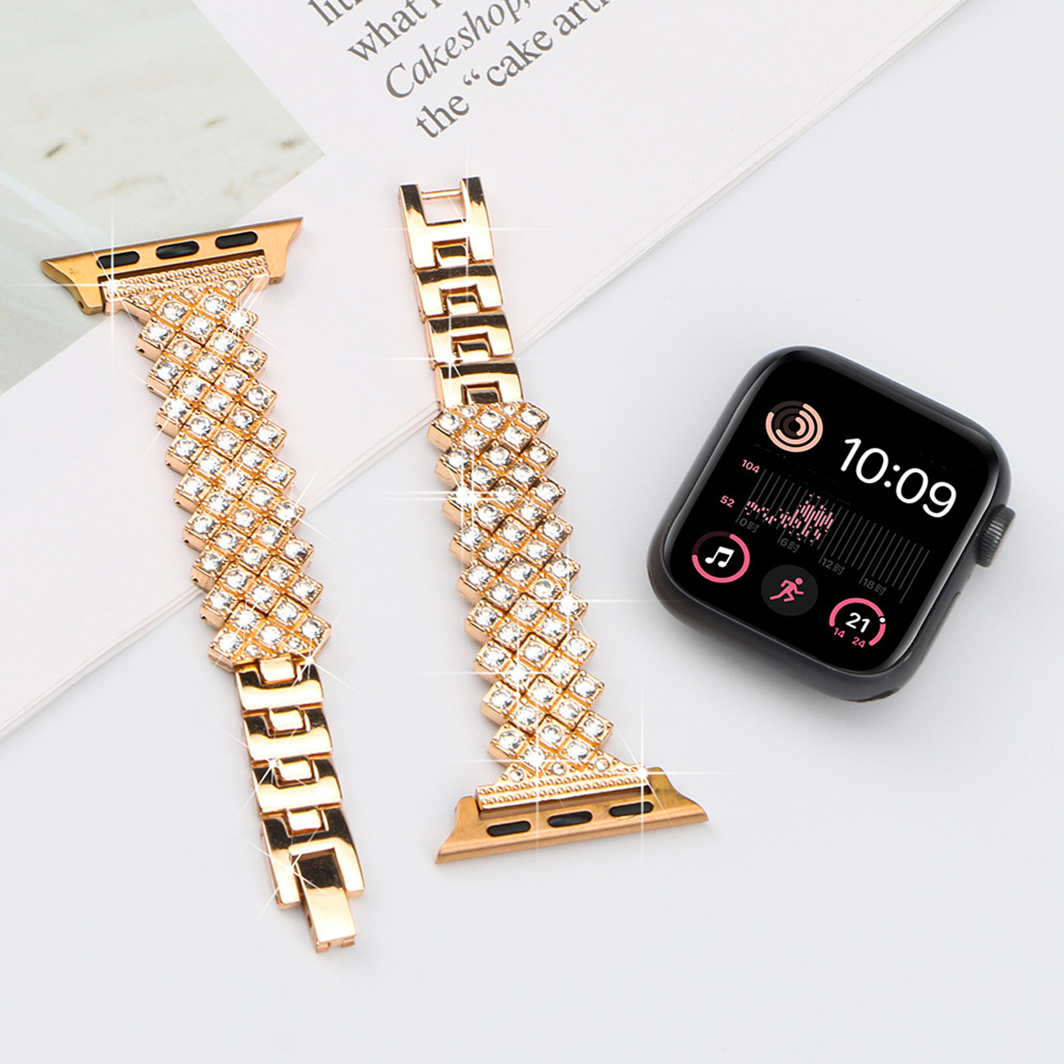 Eine Smartwatch und zwei goldene Armbänder mit Diamanten. Ein weißes Papier im Hintergrund.
