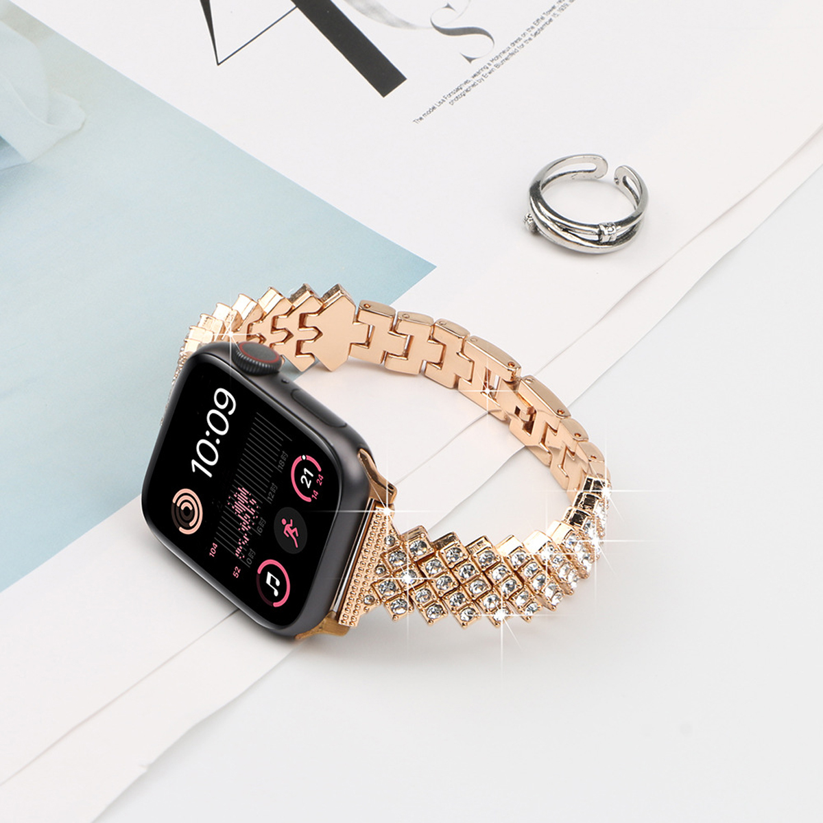 Eine roségoldene Uhr mit Diamantband liegt auf einer weißen Oberfläche mit einem Silberring.