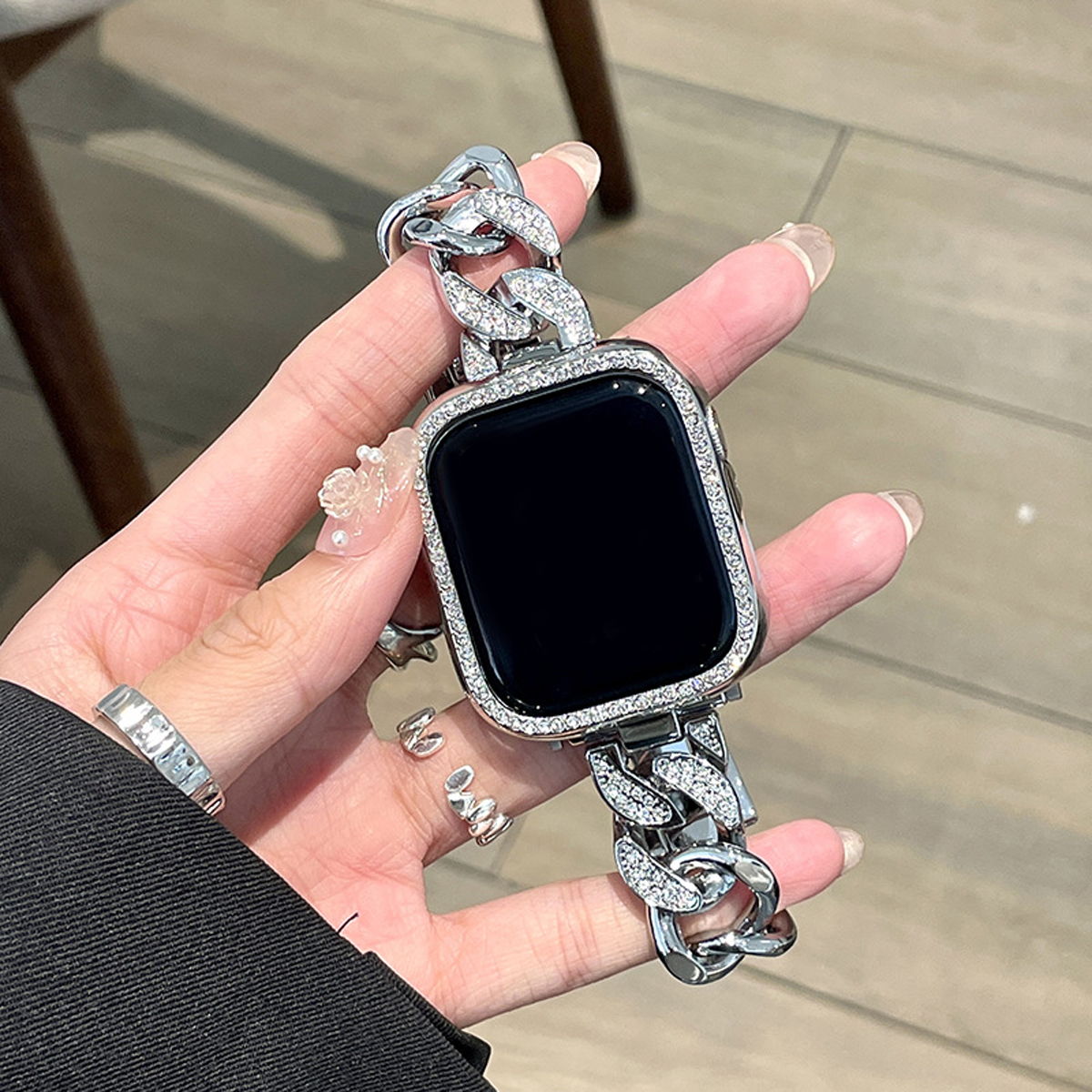 Silbernes Ketten-Uhrenarmband an einer Hand, Zifferblatt ist schwarz und hat einen Diamantrahmen.