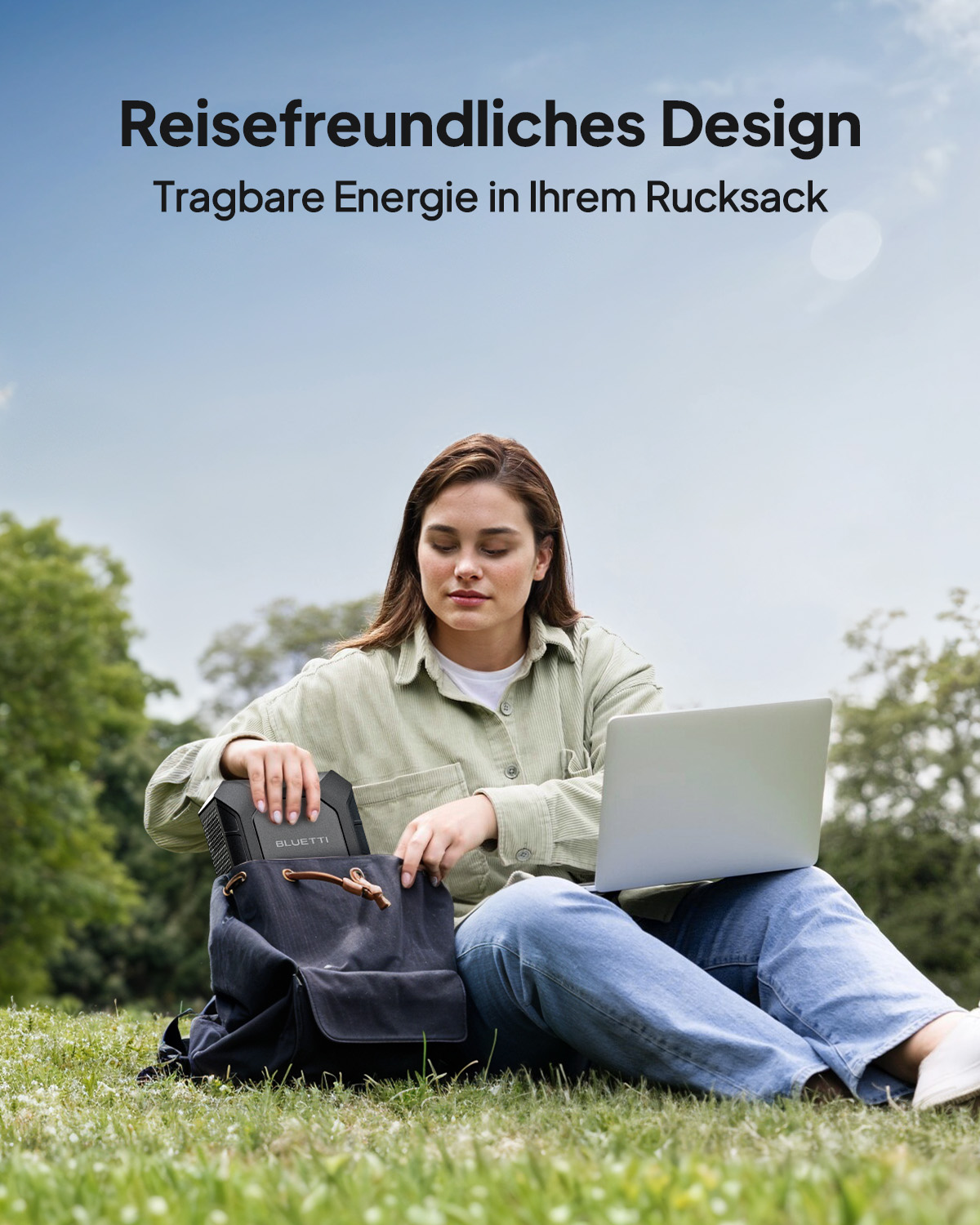 Eine Frau sitzt auf Gras mit Laptop und Rucksack, mit einer tragbaren Powerstation.