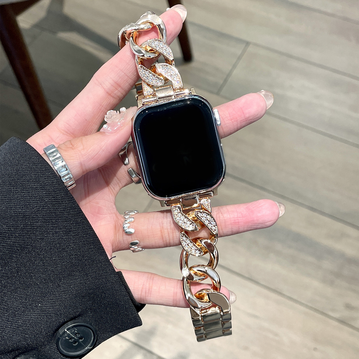 Goldenes Uhrenarmband aus Kette, gehalten von Hand mit Nagellack und Silberring.
