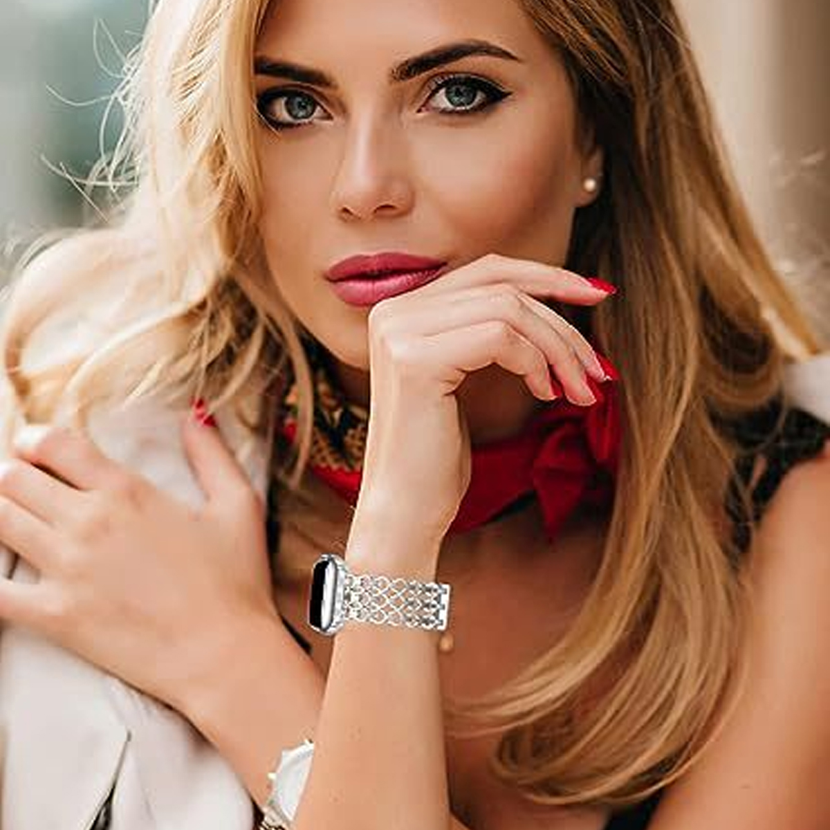 Eine Frau mit blonden Haaren, die eine Uhr mit Strasssteinen und einen roten Schal trägt.