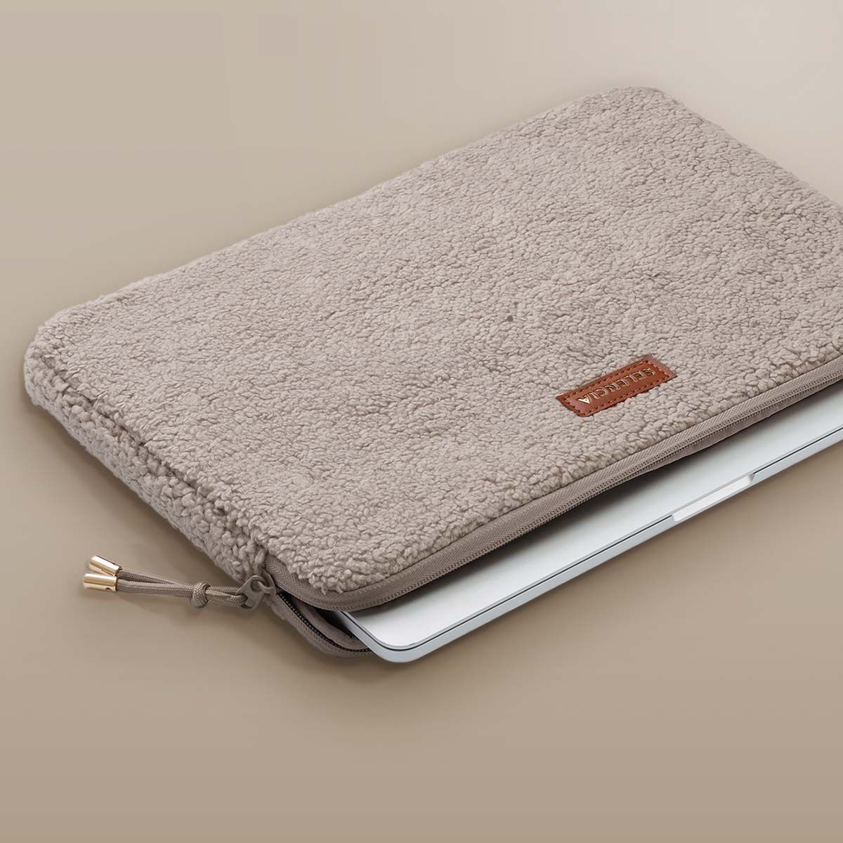 Close-up of a fluffy gray laptop sleeve with a laptop inside. Beige background.