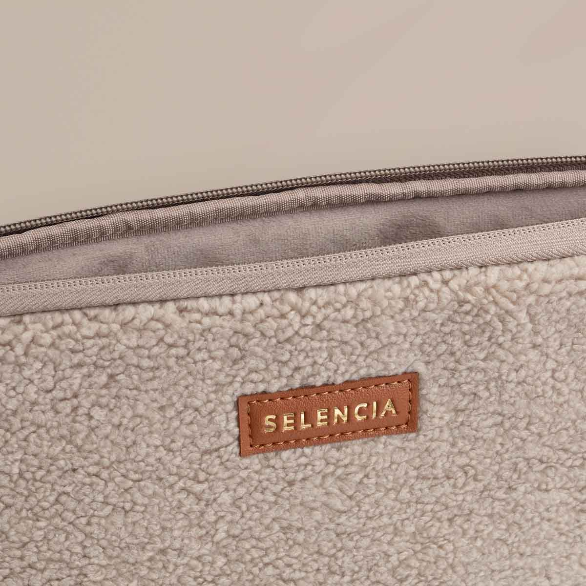 Close-up of a beige, fluffy fabric with a brown leather tag that says 'SELENCIA'.