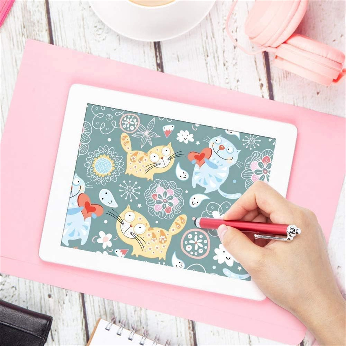 Ein Tablet zeigt einen Cartoon, eine Hand hält einen roten Stift, auf rosa Oberfläche. Pinke Kopfhörer im Hintergrund.