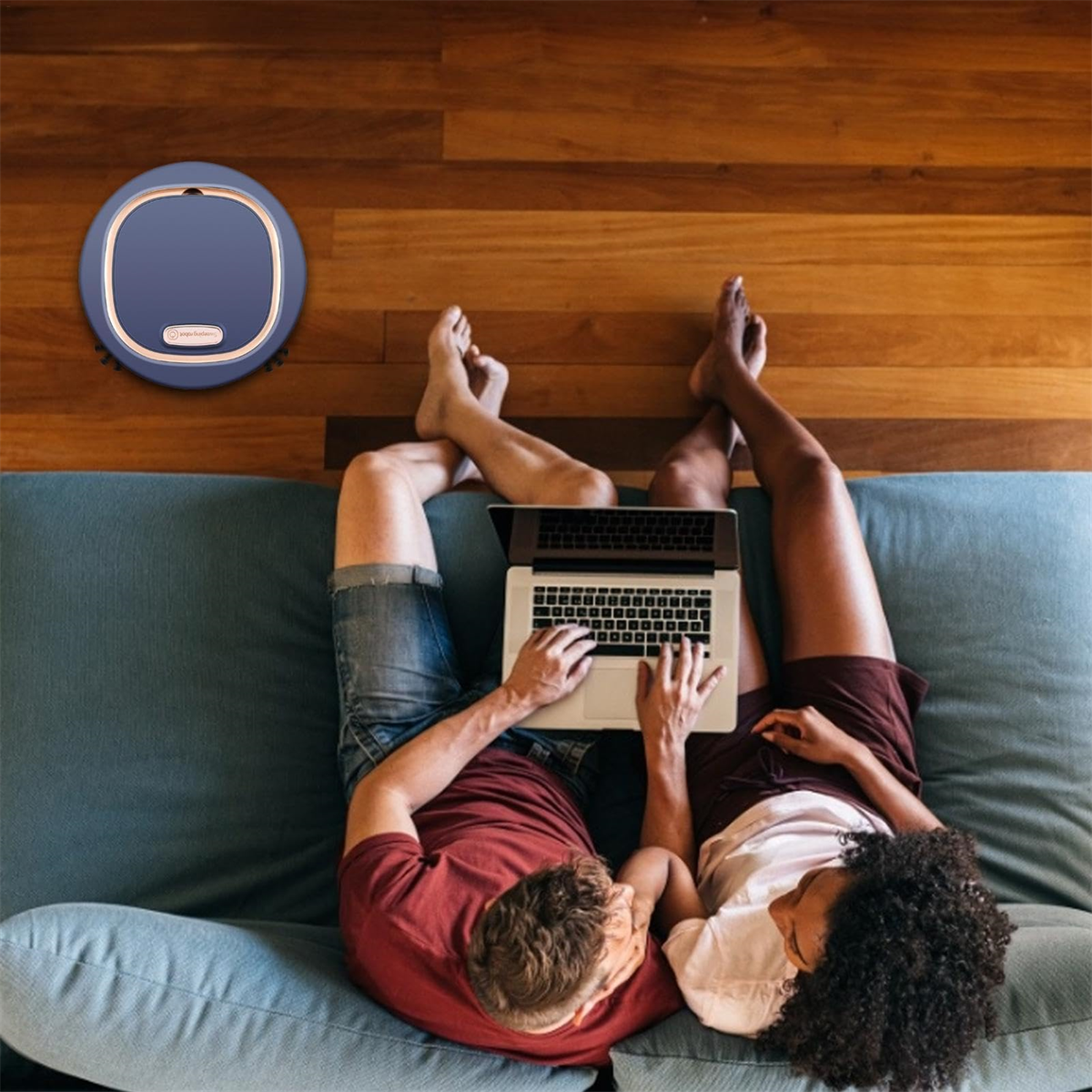 Personen liegen auf Couch, arbeiten am Laptop. Roboter-Staubsauger daneben.