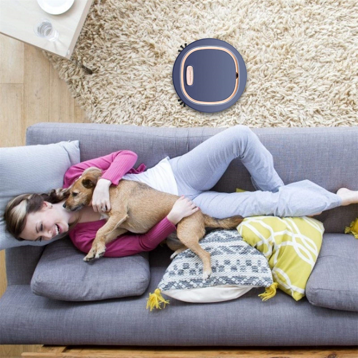 Frau und Hund entspannen sich auf einem grauen Sofa, ein Roboterstaubsauger in der Nähe.