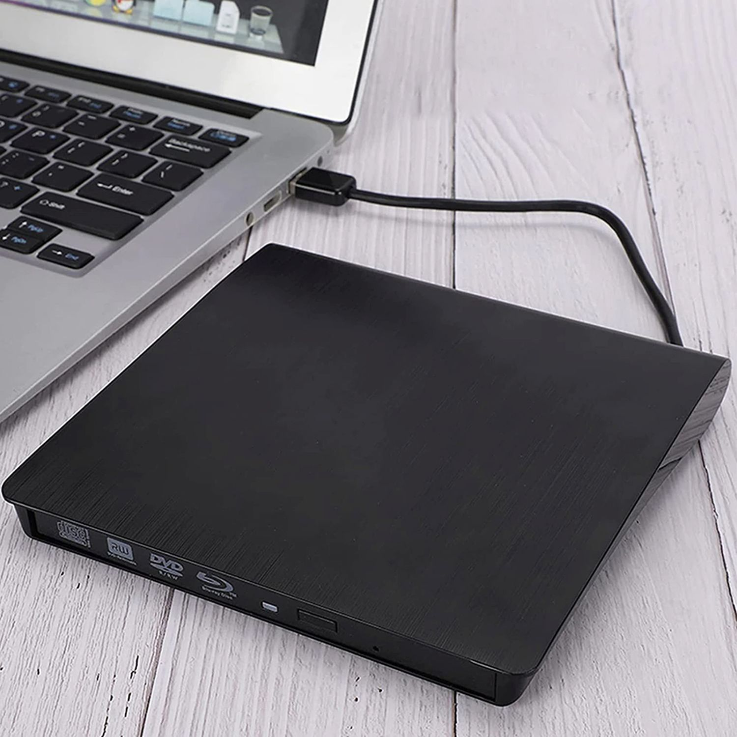 Schwarzes externes DVD-Laufwerk, per USB mit Laptop verbunden, auf hellem Holz.