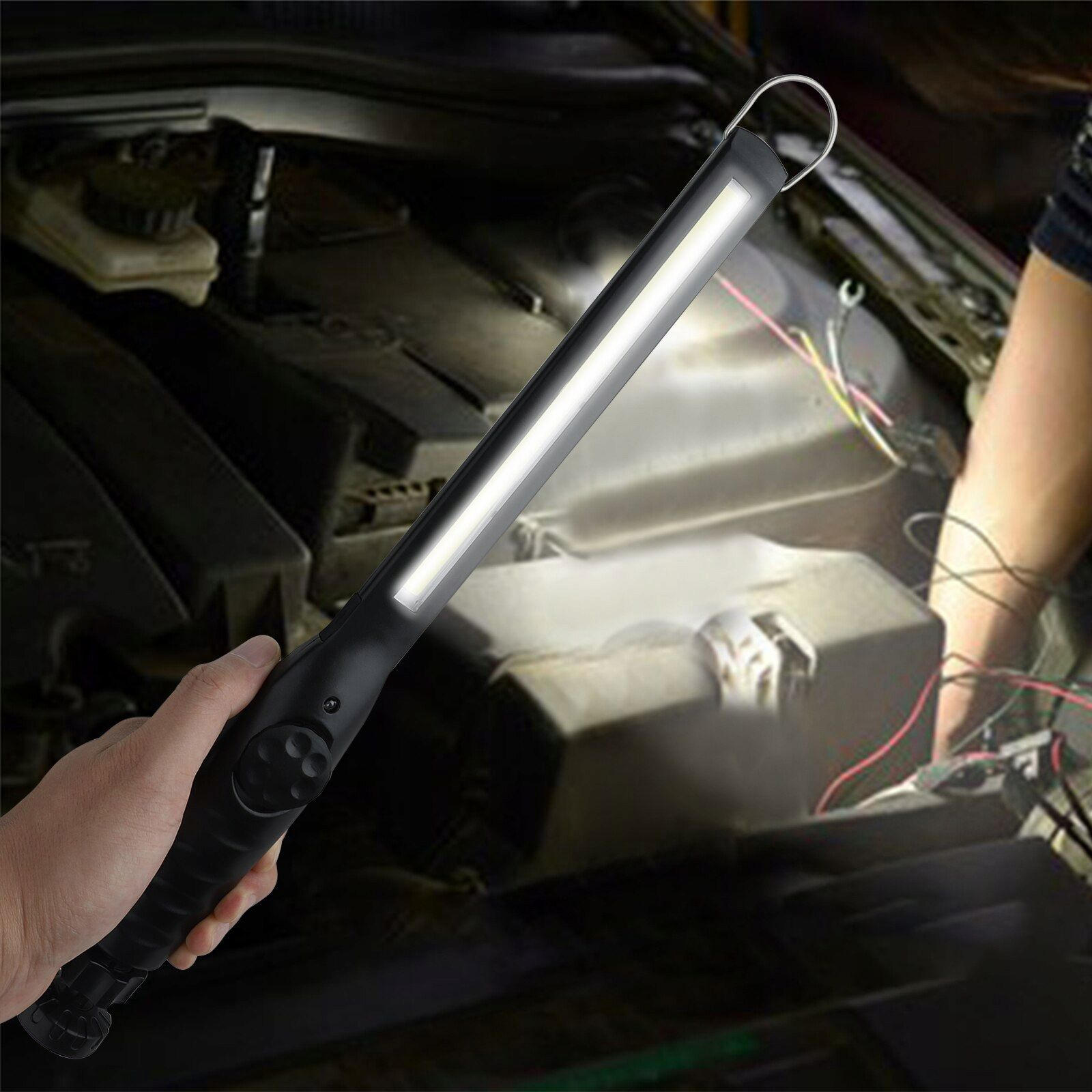 Schwarze LED-Arbeitsleuchte in der Hand, die den Motorraum eines Autos ausleuchtet.
