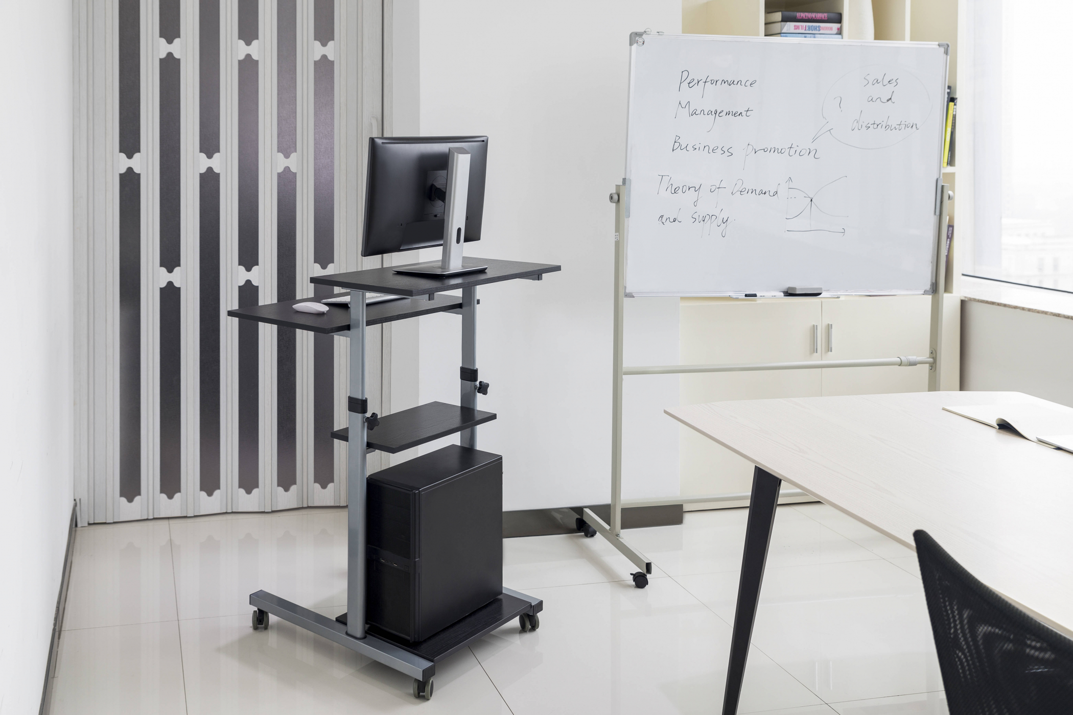 A rolling cart with a computer, monitor, and a whiteboard. A desk and chair are nearby. White background.