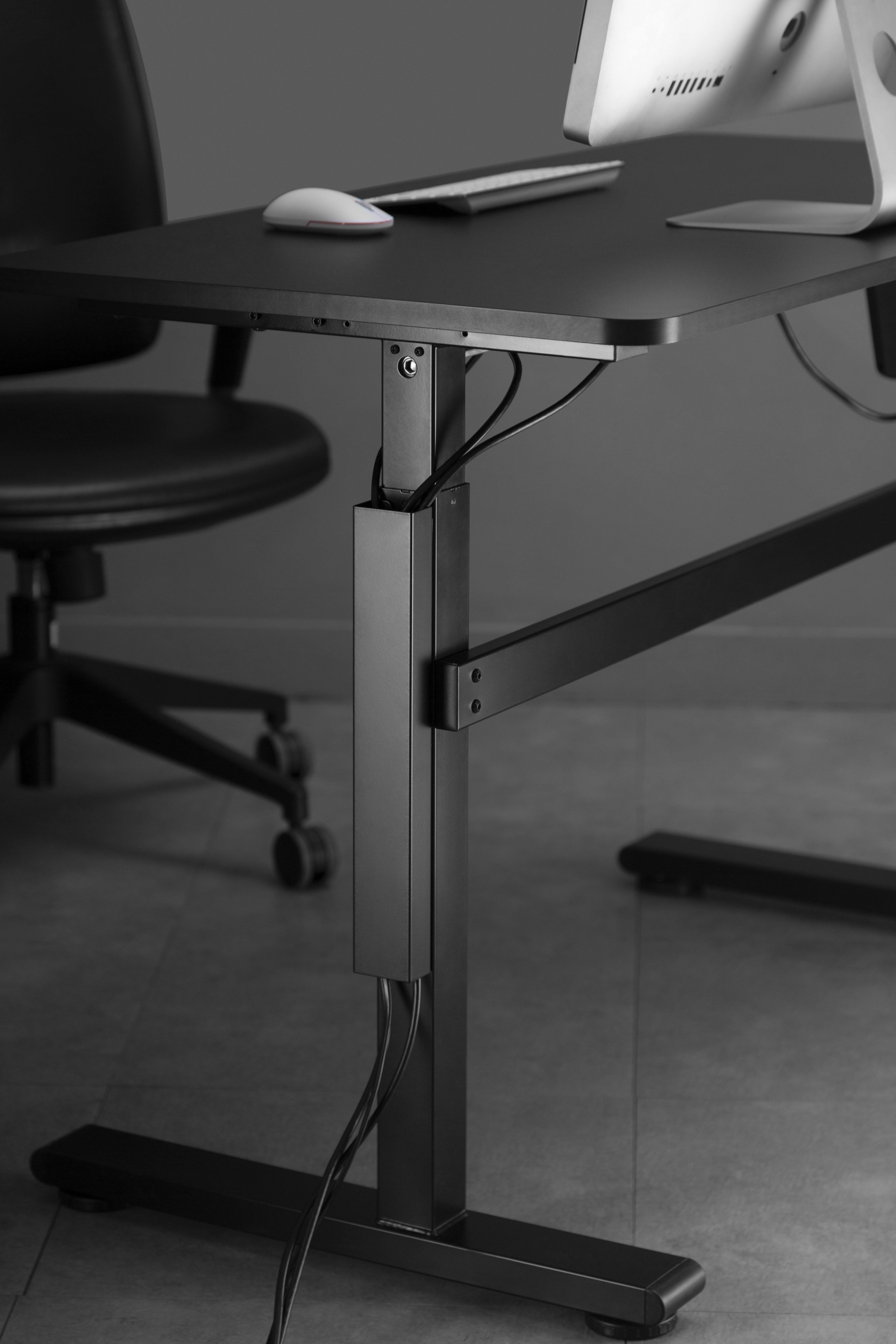 Zwart bureau met computerscherm, muis en kabels. Een zwarte stoel links.