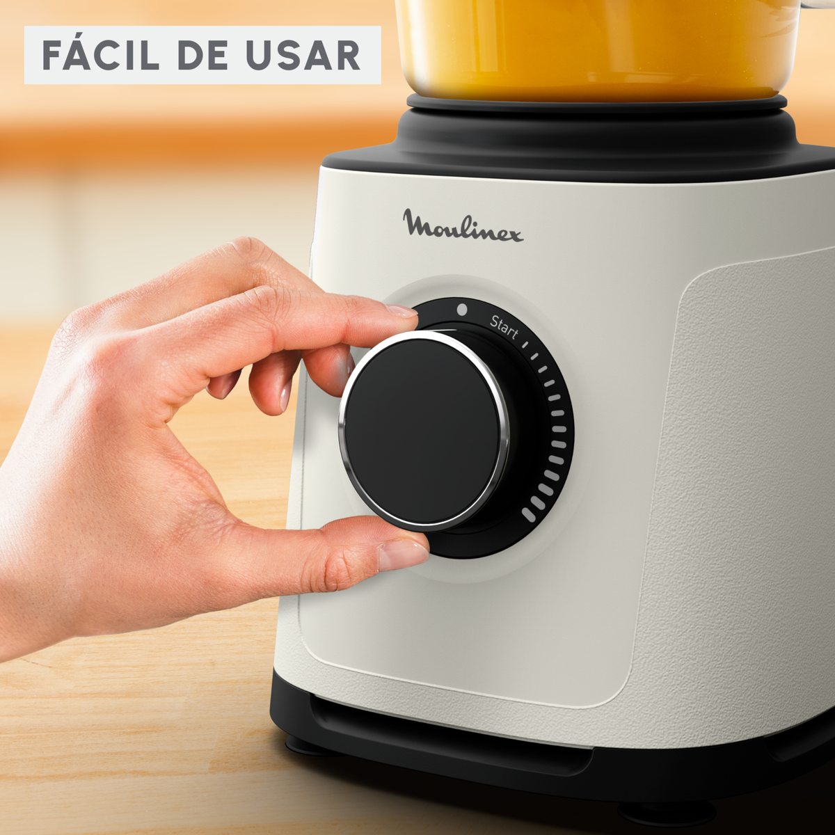 Una mano girando un dial negro en una licuadora blanca, con el texto 'FÁCIL DE USAR' arriba.