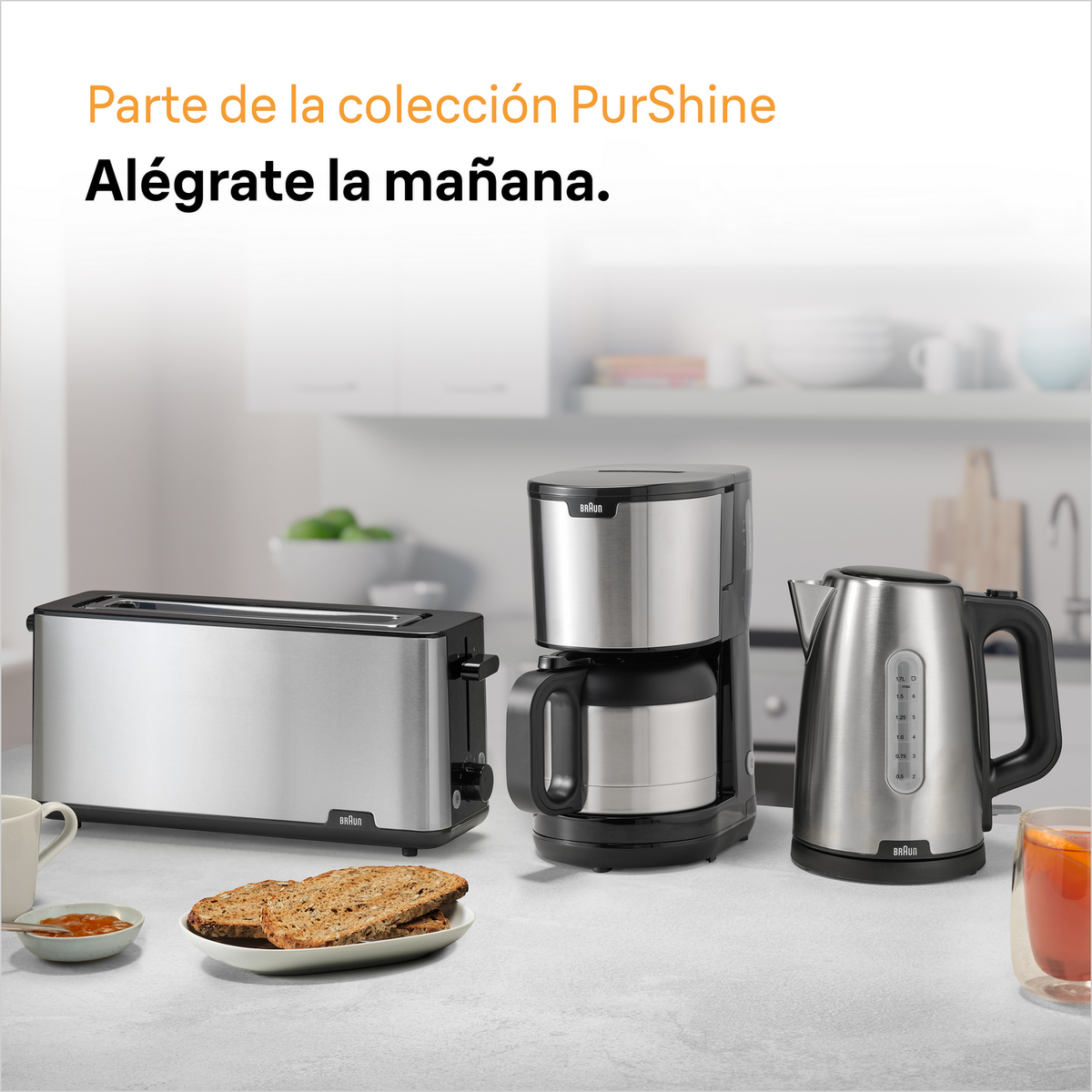 Sprzęt kuchenny: toster, ekspres do kawy i czajnik. Talerz z chlebem i marmoladą. Tekst po hiszpańsku.