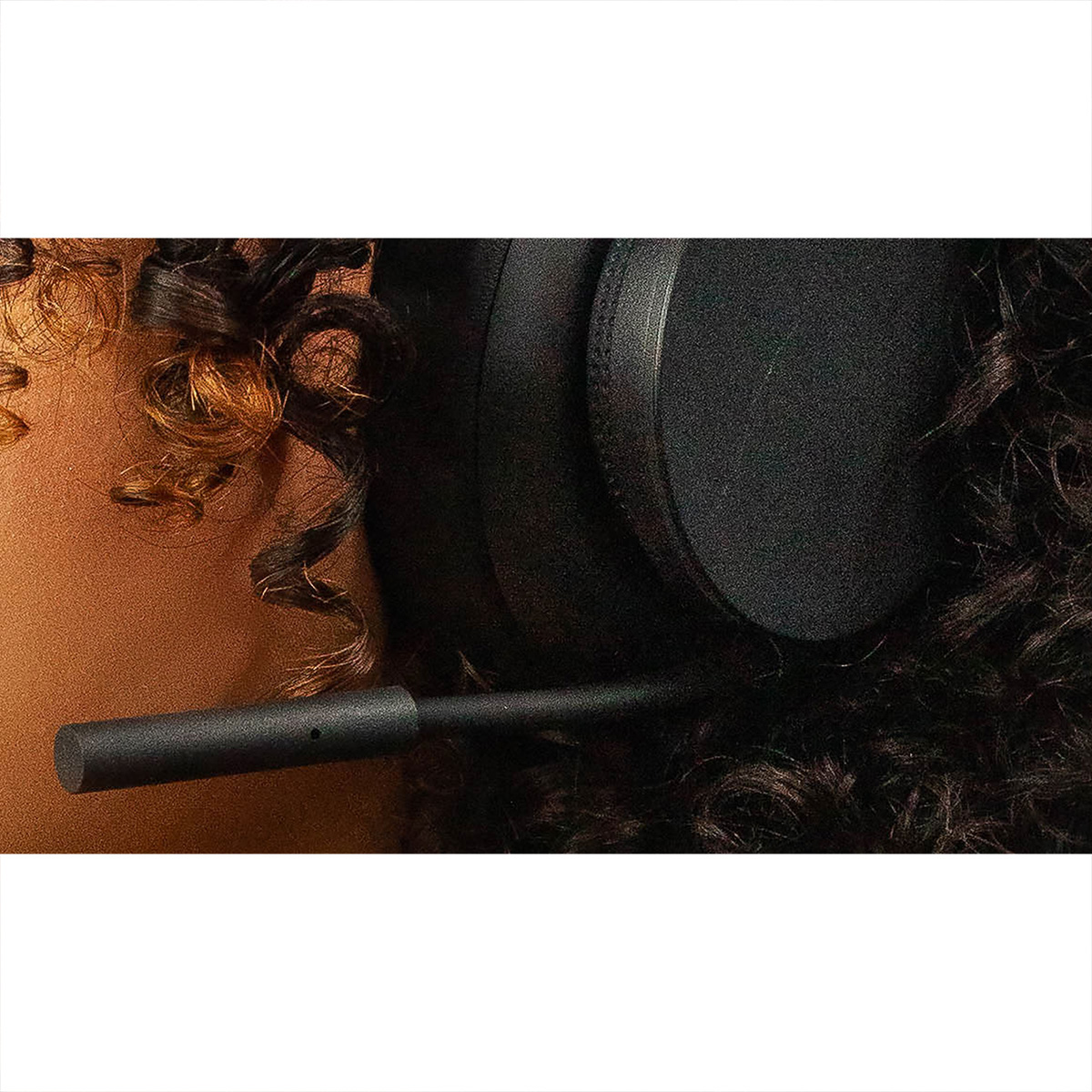 Cuffie nere con microfono sui capelli ricci scuri di una persona. Primo piano.