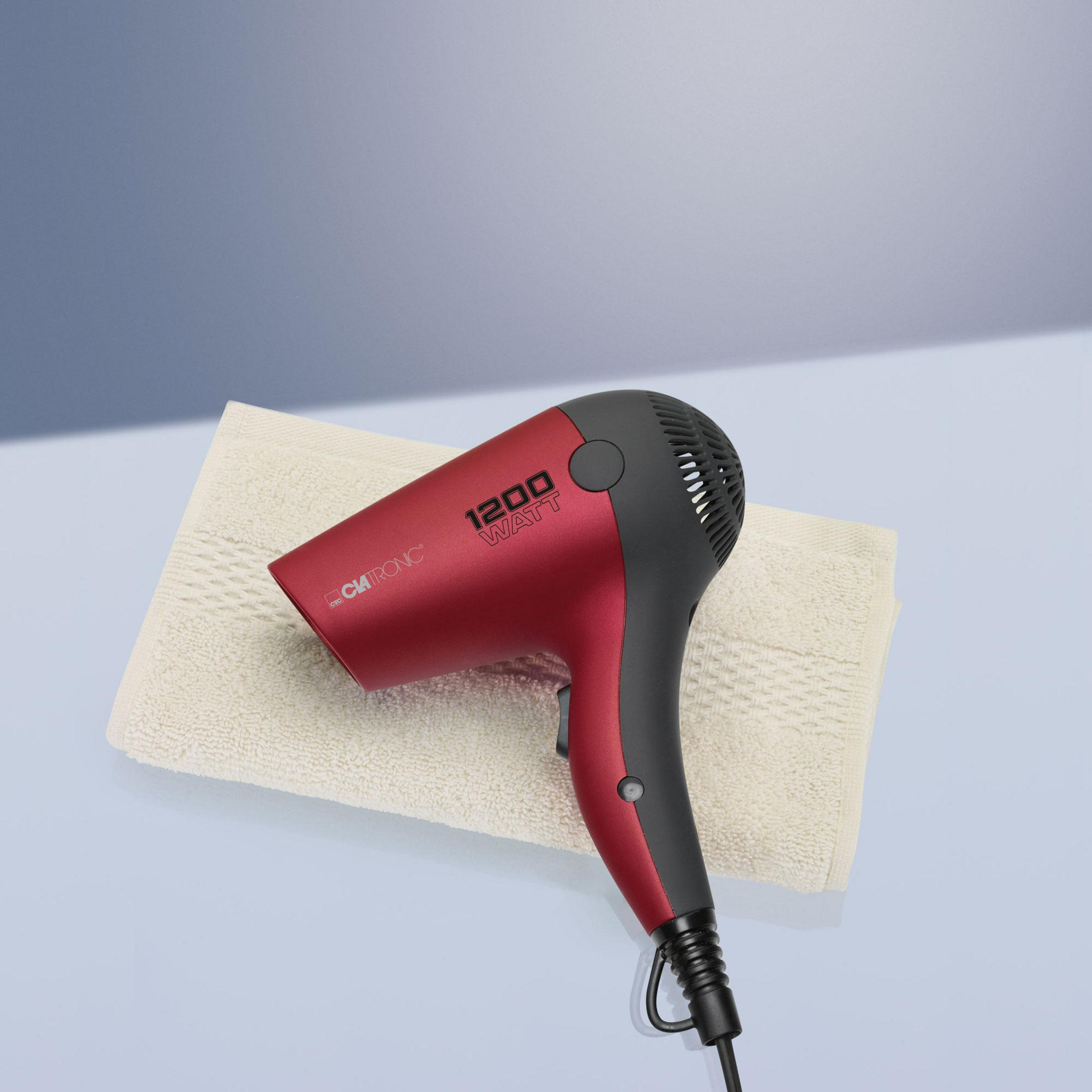 Secador de pelo rojo y negro sobre una toalla. El fondo es una superficie azul claro.
