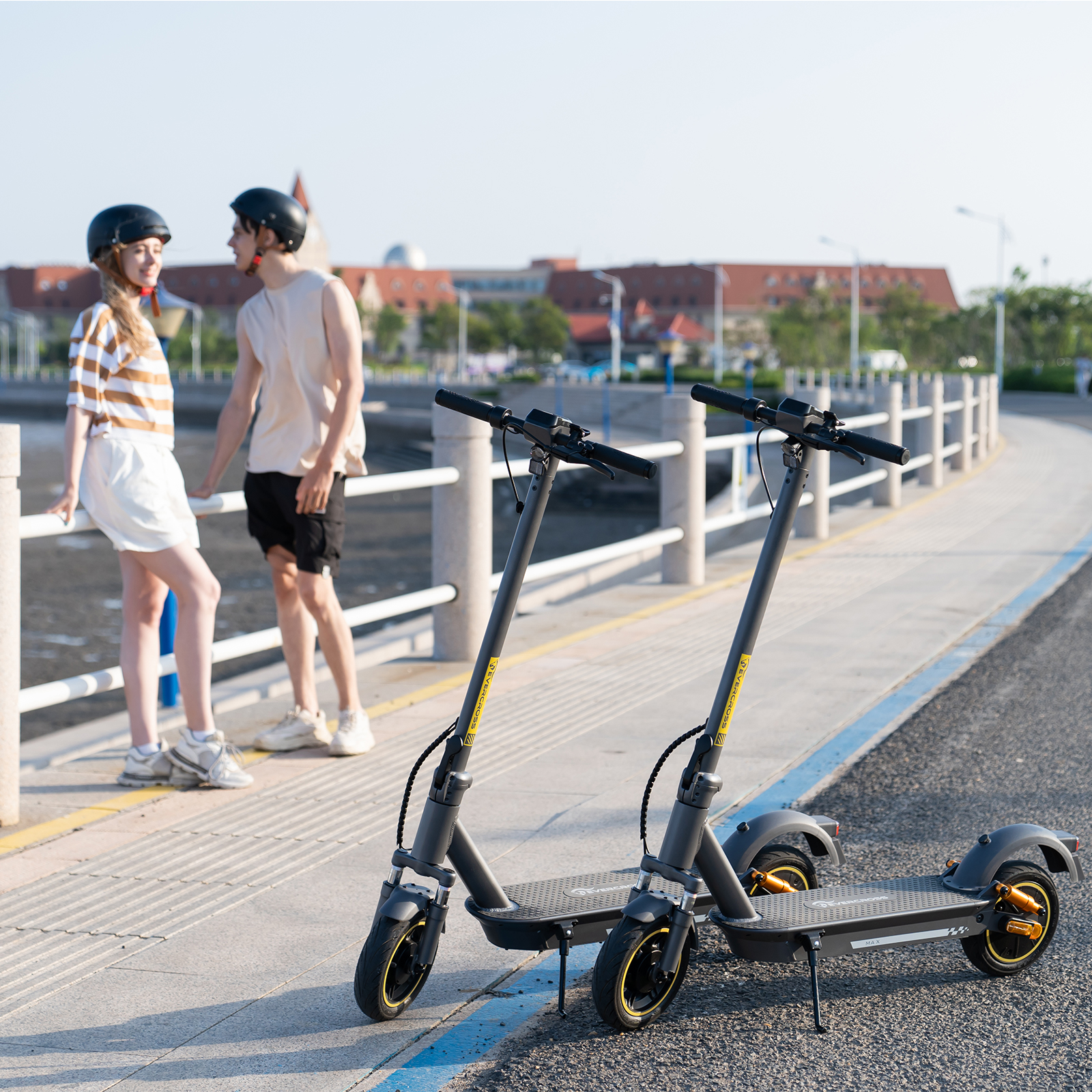 Zwei Elektroroller auf einem gepflasterten Weg, zwei Personen stehen in der Nähe, sonniger Tag.