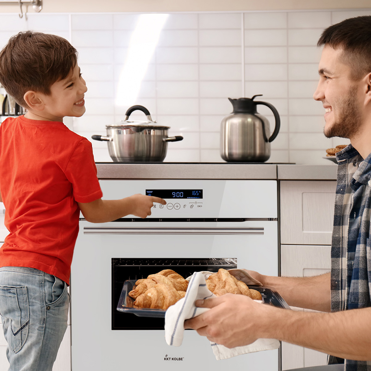 Ein Junge und ein Mann sind in einer Küche. Der Junge zeigt auf den Backofen, der Mann hält Croissants.
