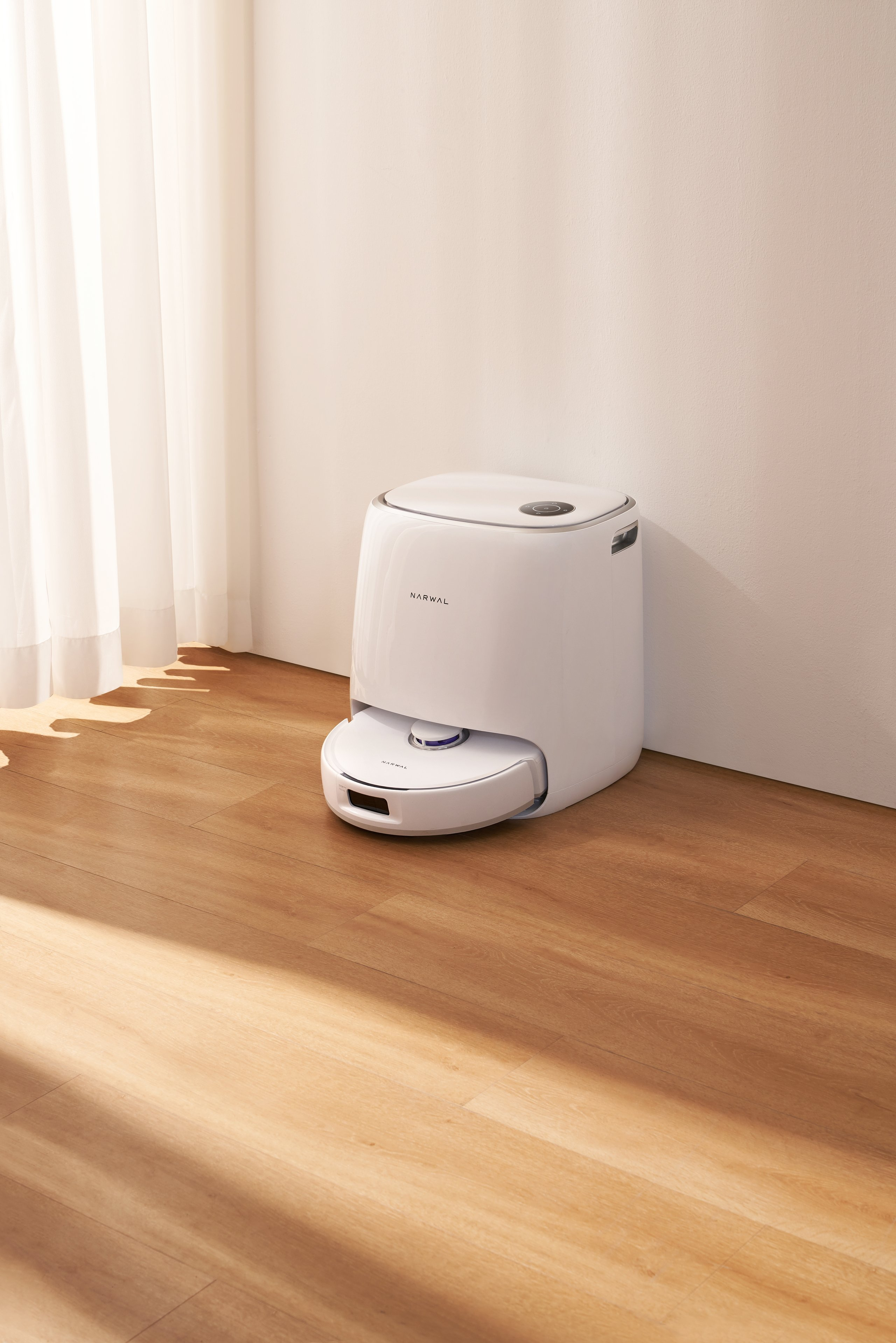 Biały odkurzacz automatyczny na drewnianej podłodze obok ściany. Nowoczesny design.