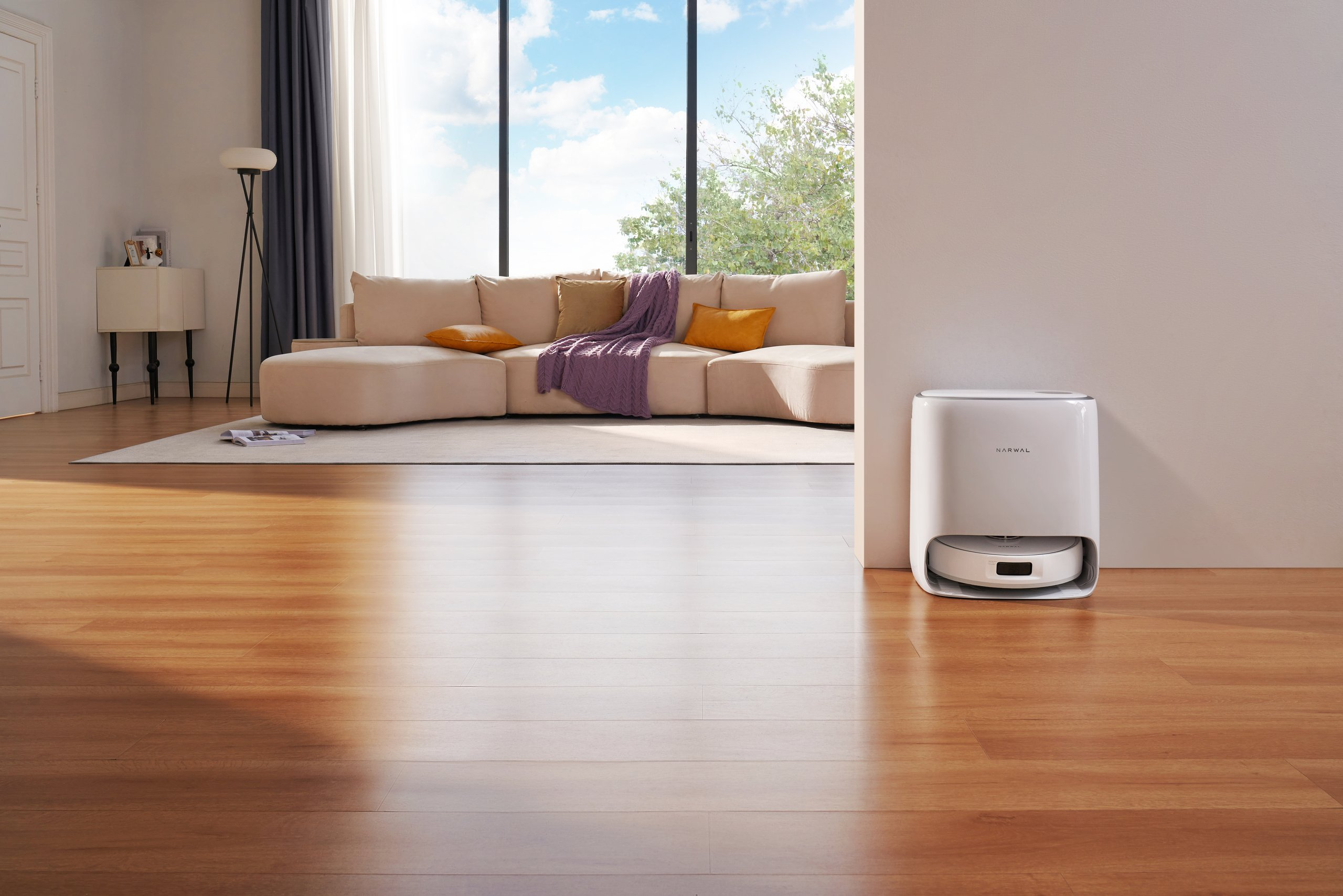 Pokój z robotem odkurzającym i sofą. Podłoga jest drewniana, a pokój dobrze oświetlony.