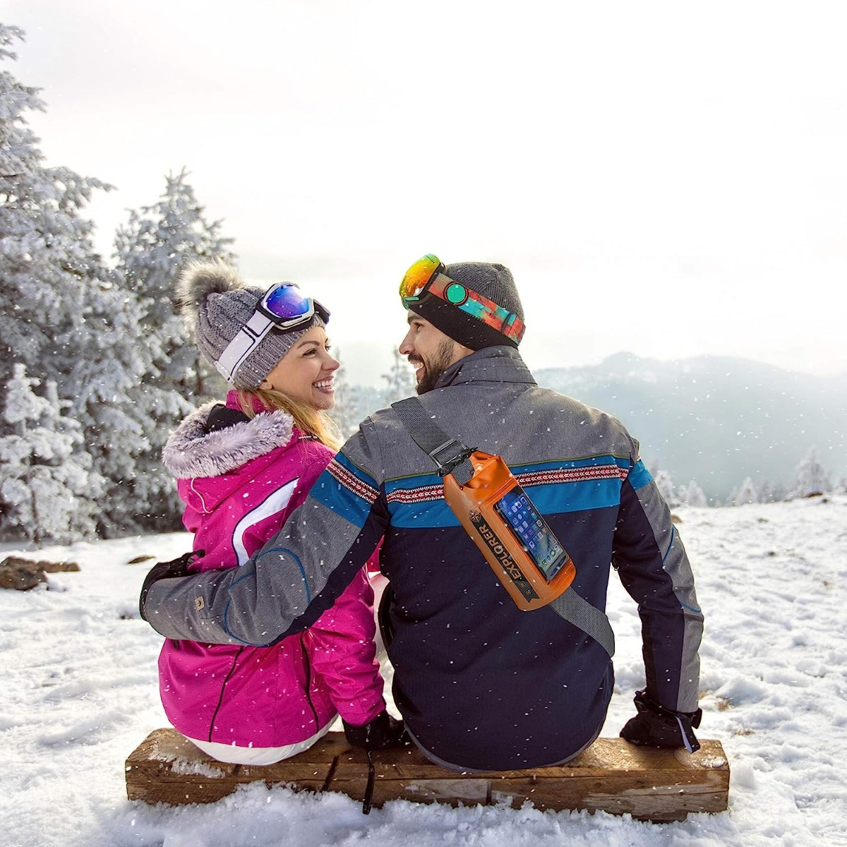 Pareja sentada en madera en la nieve. Hombre con teléfono en funda.