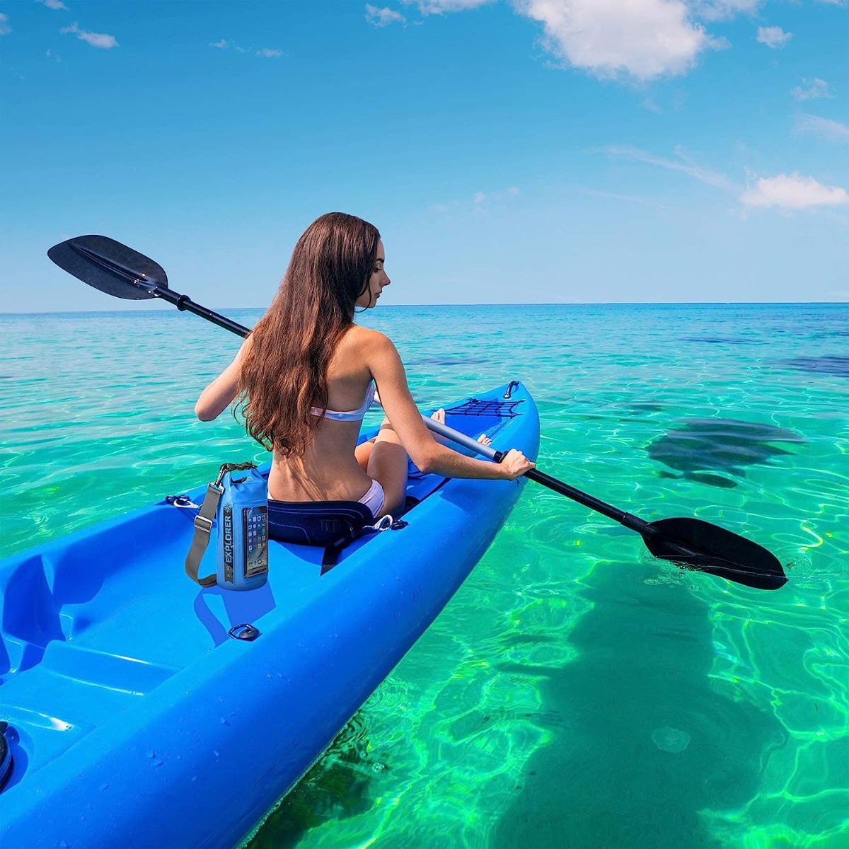Mujer en kayak azul, agua clara, cielo azul. Escena tranquila, día soleado.