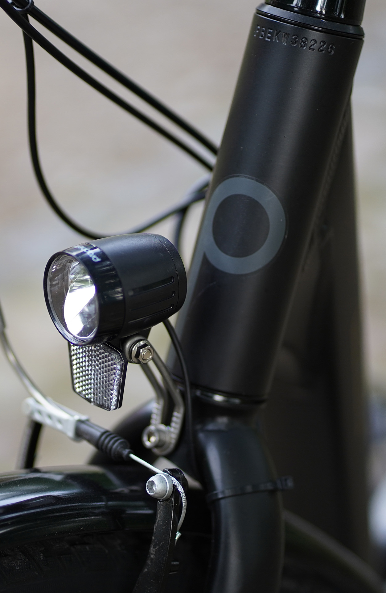 Nahaufnahme eines schwarzen Fahrradrahmens mit Scheinwerfer und Reflektor. Kabel und Bremse sind ebenfalls sichtbar, mit verschwommenem Hintergrund.