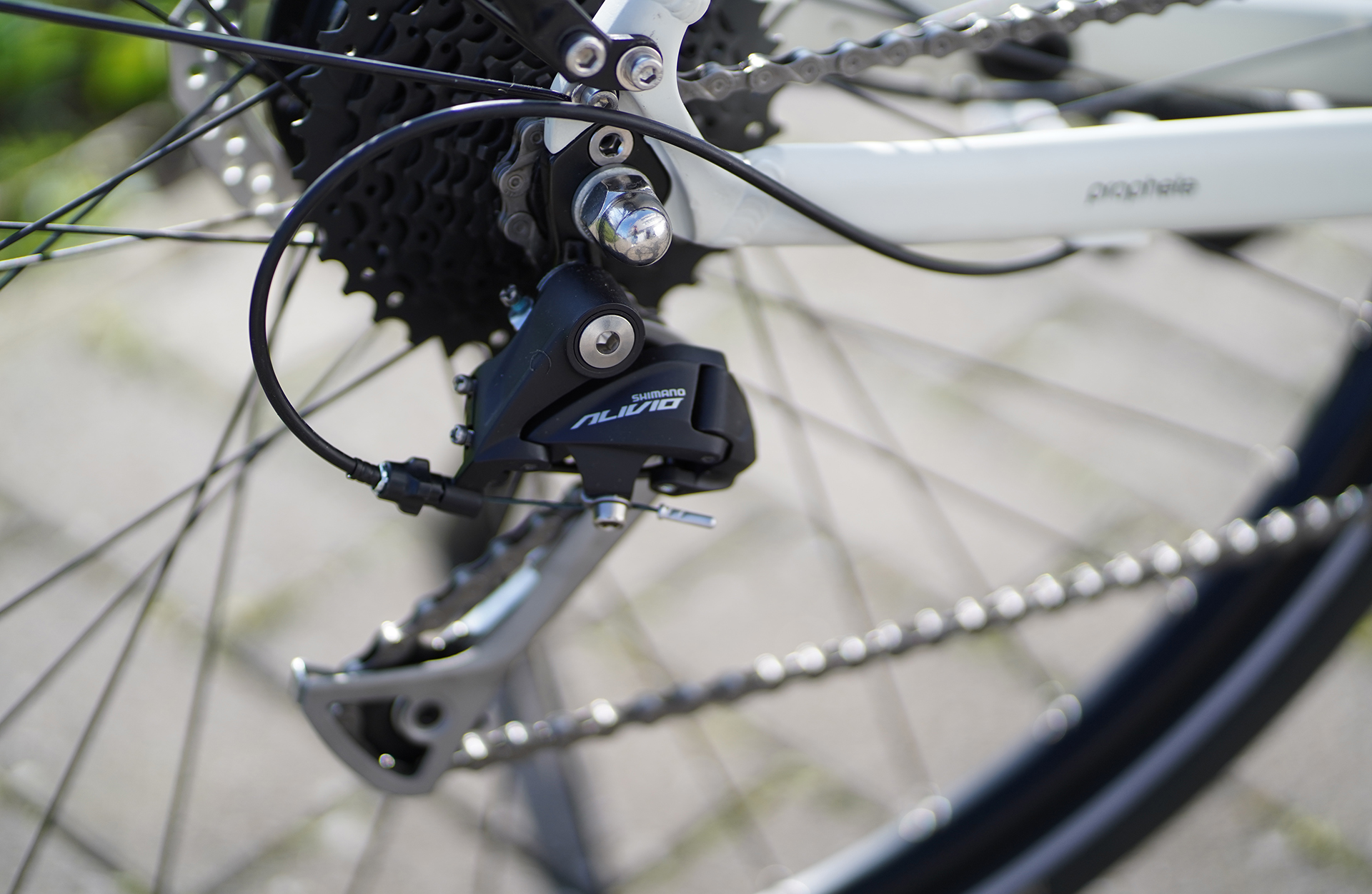 Nahaufnahme eines Fahrrad-Schaltwerks mit Kette und weißem Rahmen.